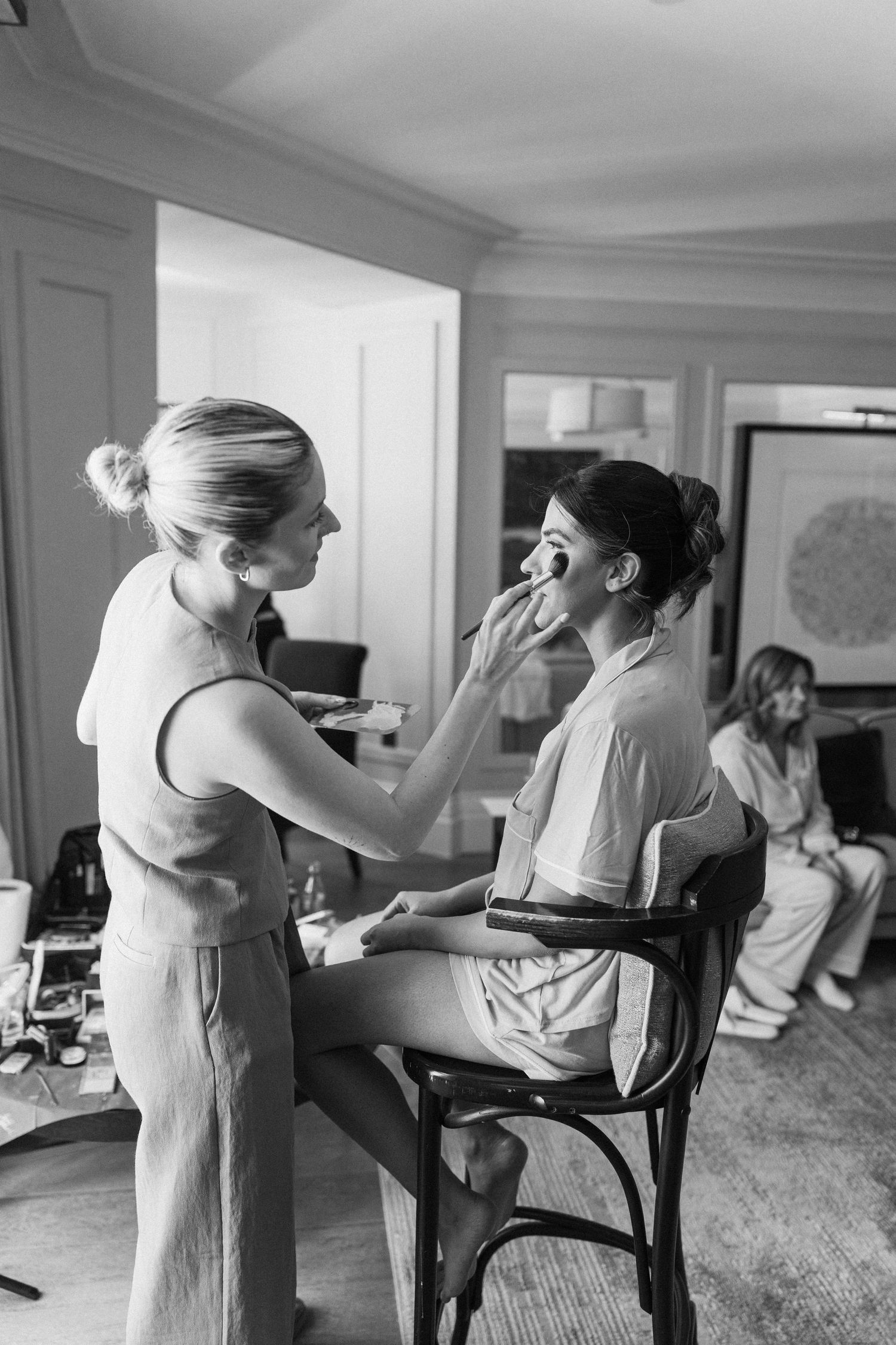 Black and white photo of a makeup artist applying foundation to a bride during wedding morning preparations.