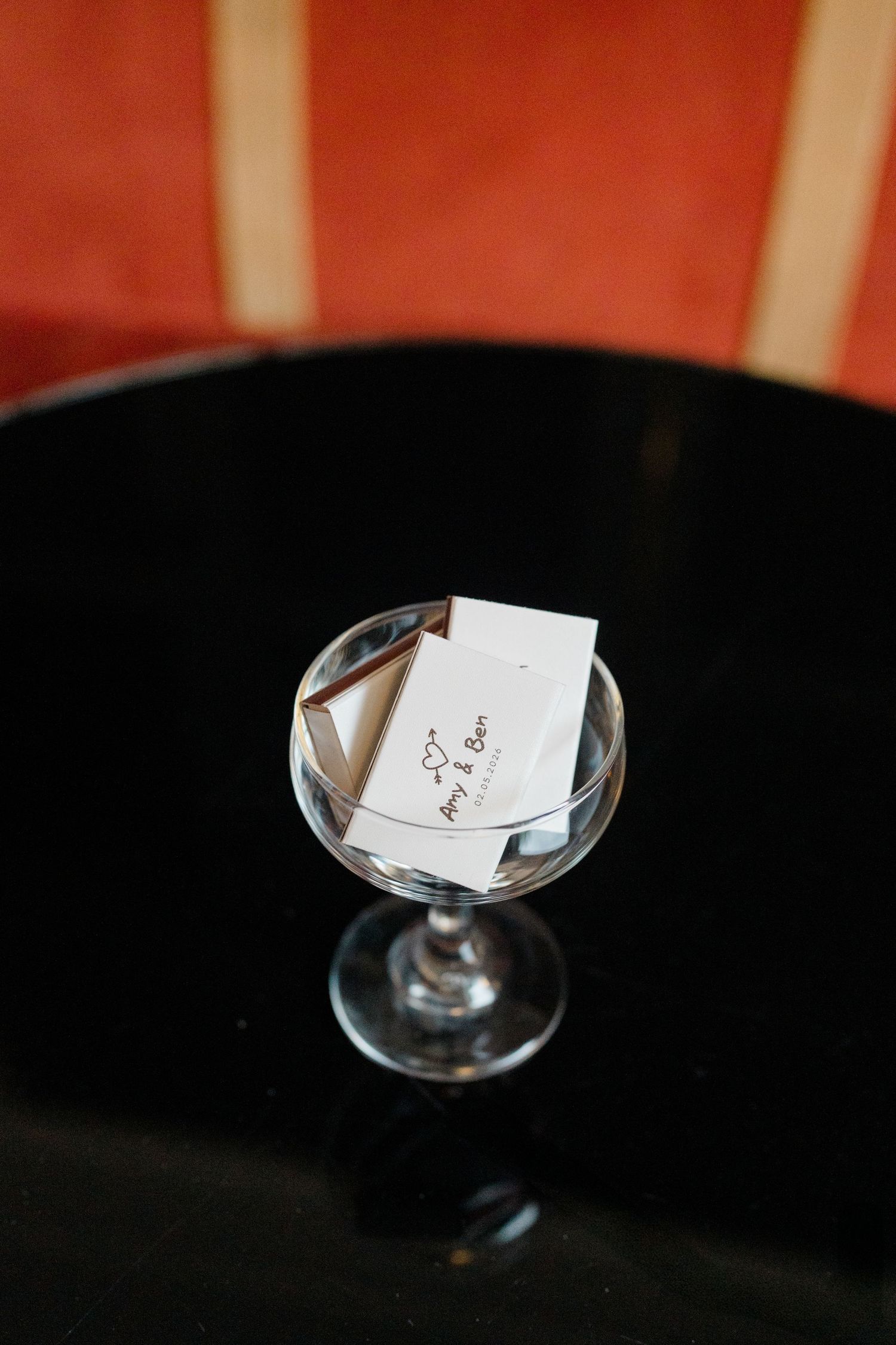 A crystal martini glass holding a small wedding place card on a black reflective table.