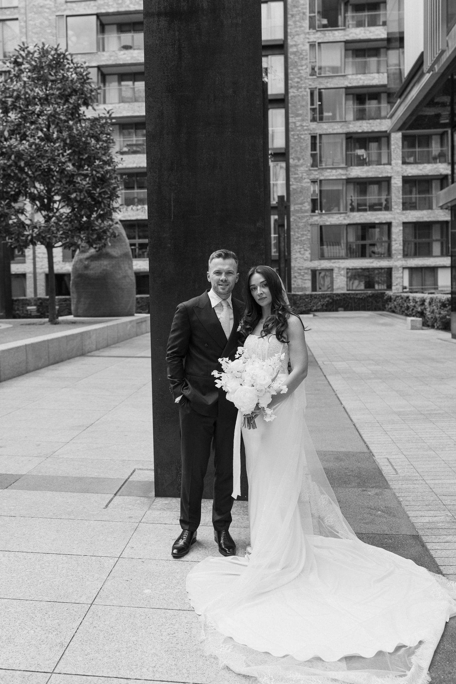 Black and white portrait of a bride and groom posing together in an urban setting.