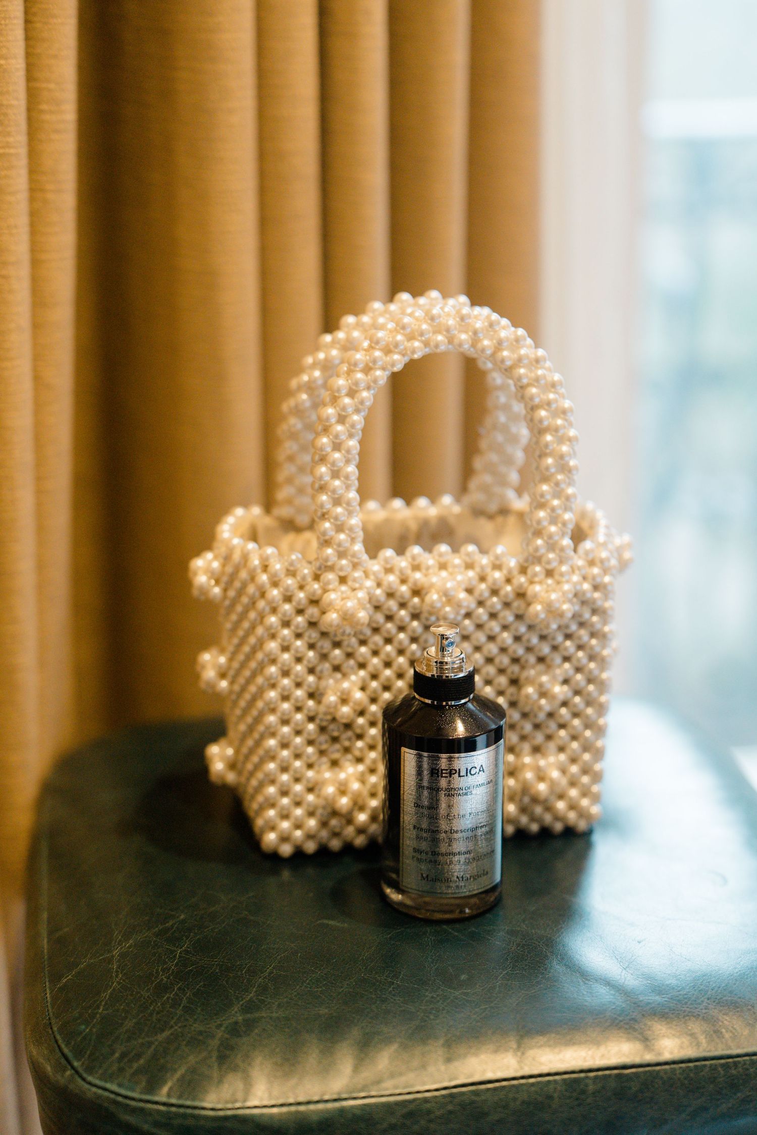 Pearl beaded handbag with Maison Margiela Replica perfume bottle on green leather surface.