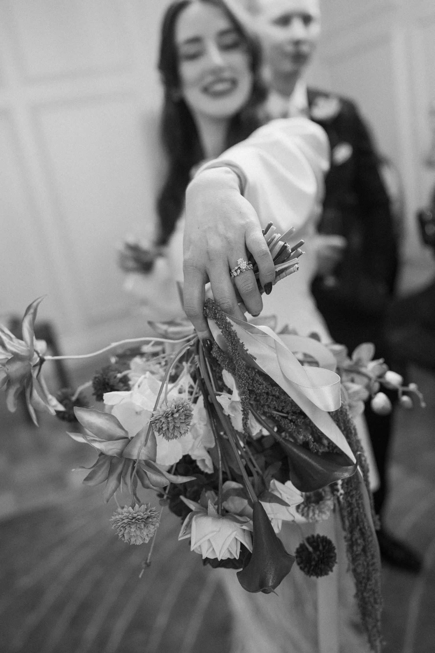 Close-up black and white photo of a bride holding a wildflower bouquet with a diamond ring visible.
