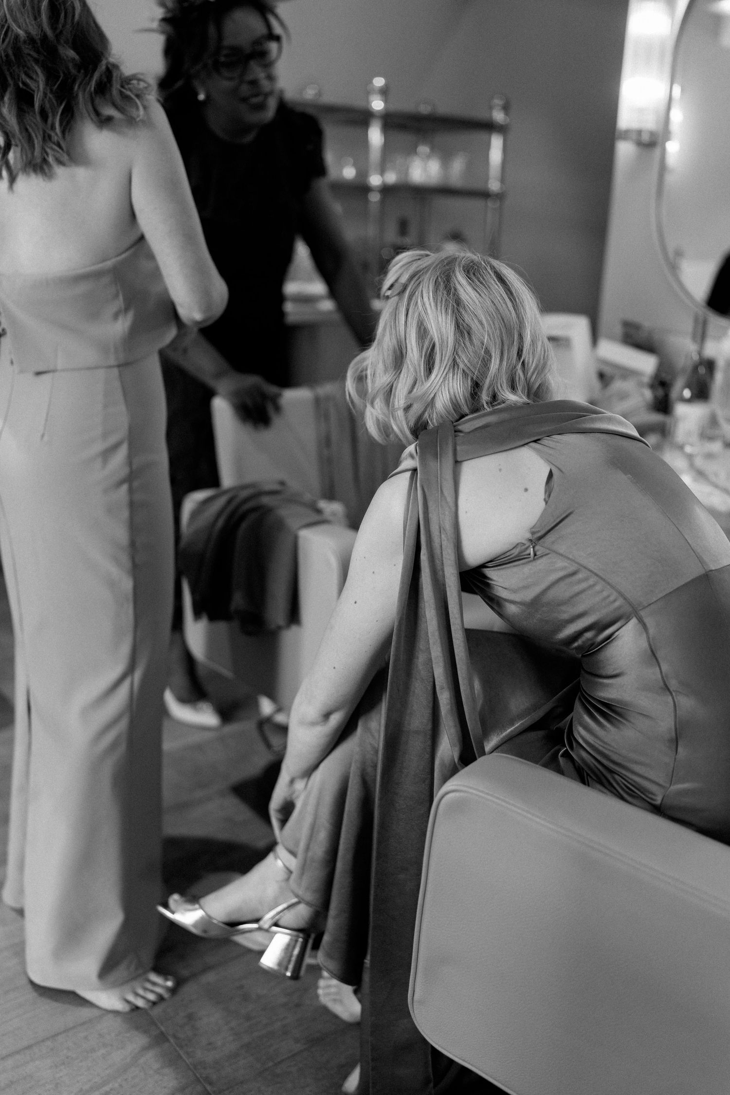 Bridesmaid adjusting heels while getting ready in black and white bridal preparation photo.