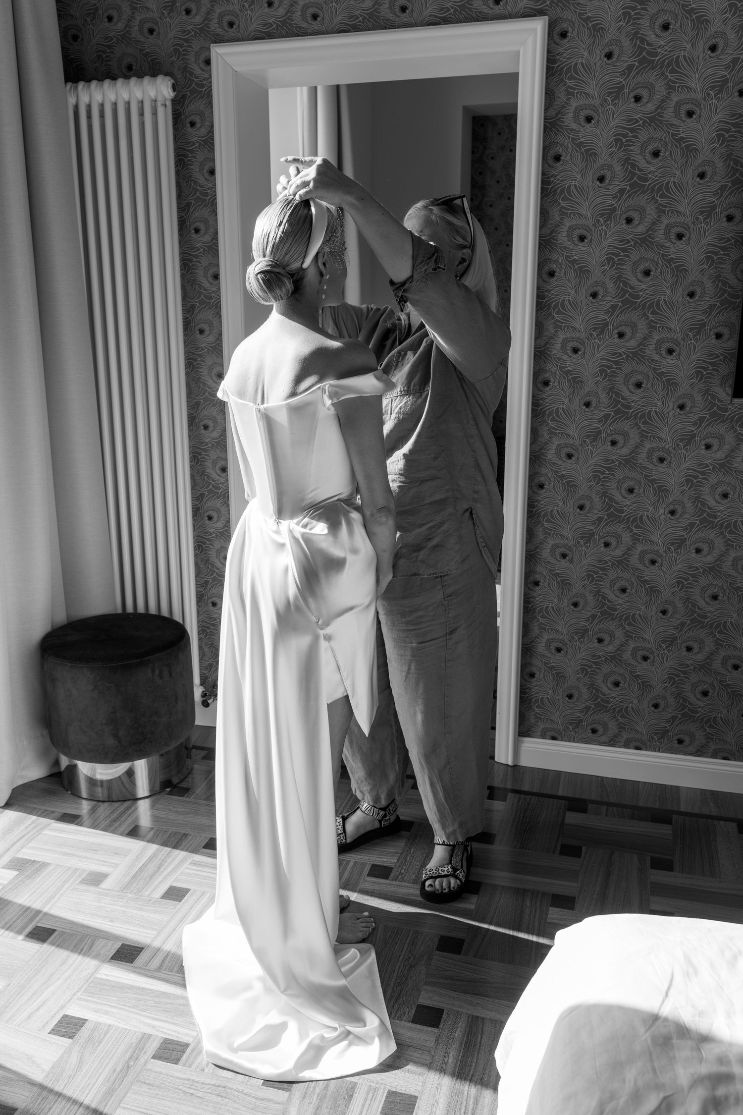 Black and white photo of bride getting hair arranged in elegant hotel room before wedding.