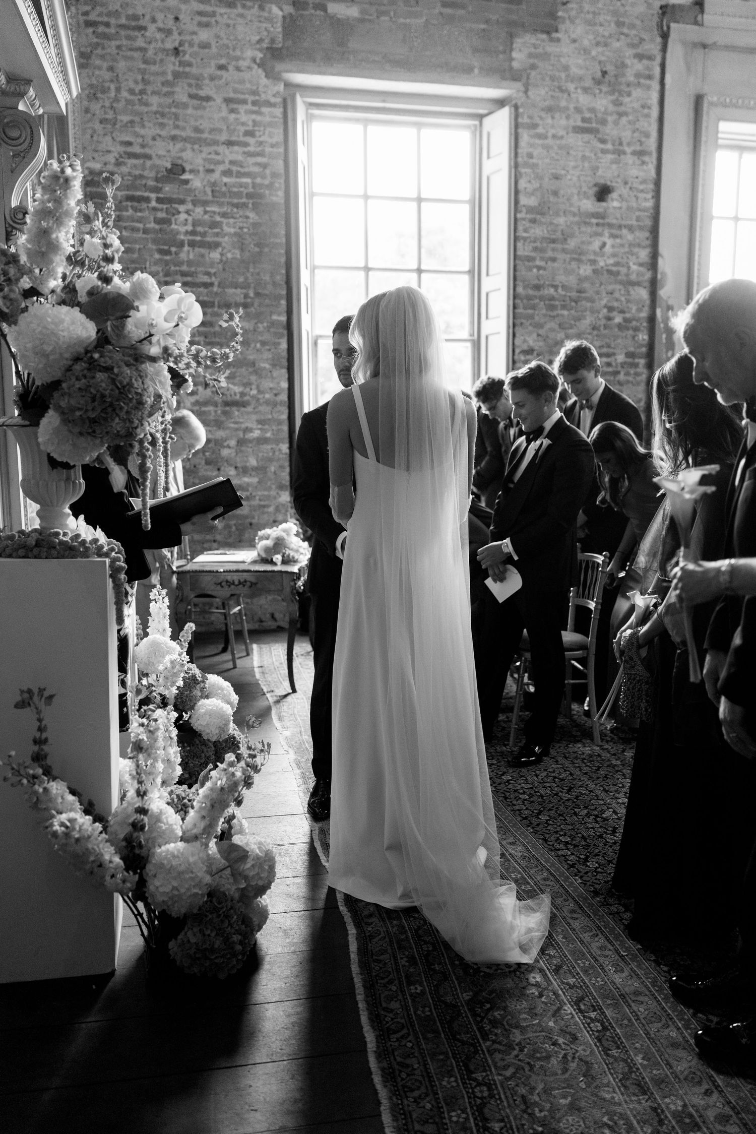 Black and white rear view of bride in veil standing at altar with groom.