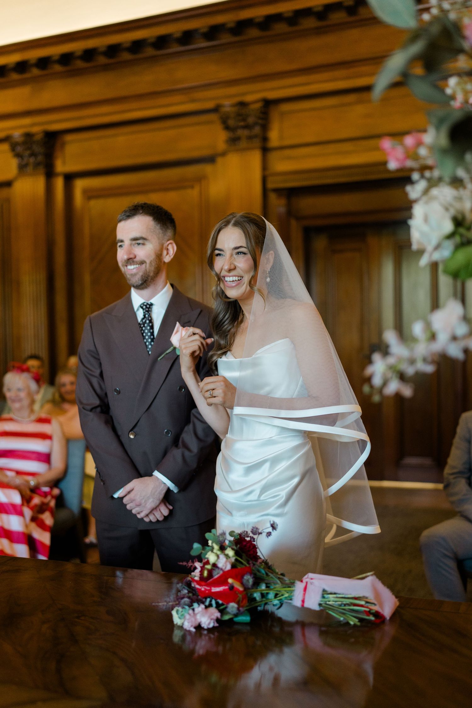 Smiling bride and groom stand at the altar during their wedding ceremony in an elegant wood-paneled room.