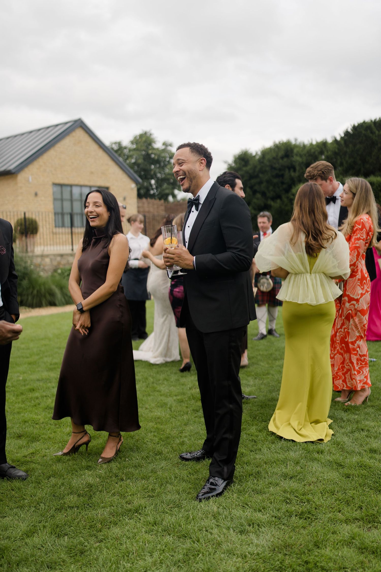 Wedding guests laugh and mingle on lawn during outdoor cocktail hour reception.
