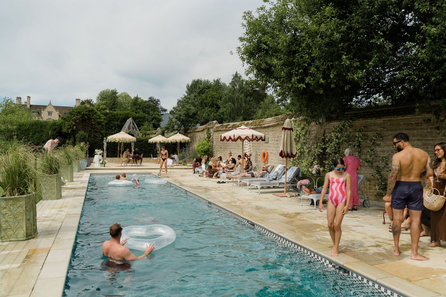 Guests relaxing and swimming at an elegant outdoor pool with loungers and thatched parasols at a venue.
