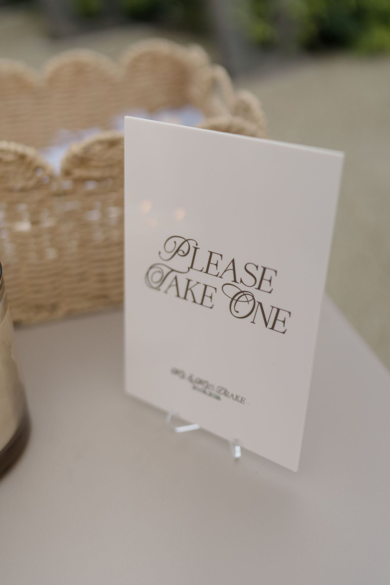 Elegant white wedding sign reading Please Take One displayed on acrylic stand on table.