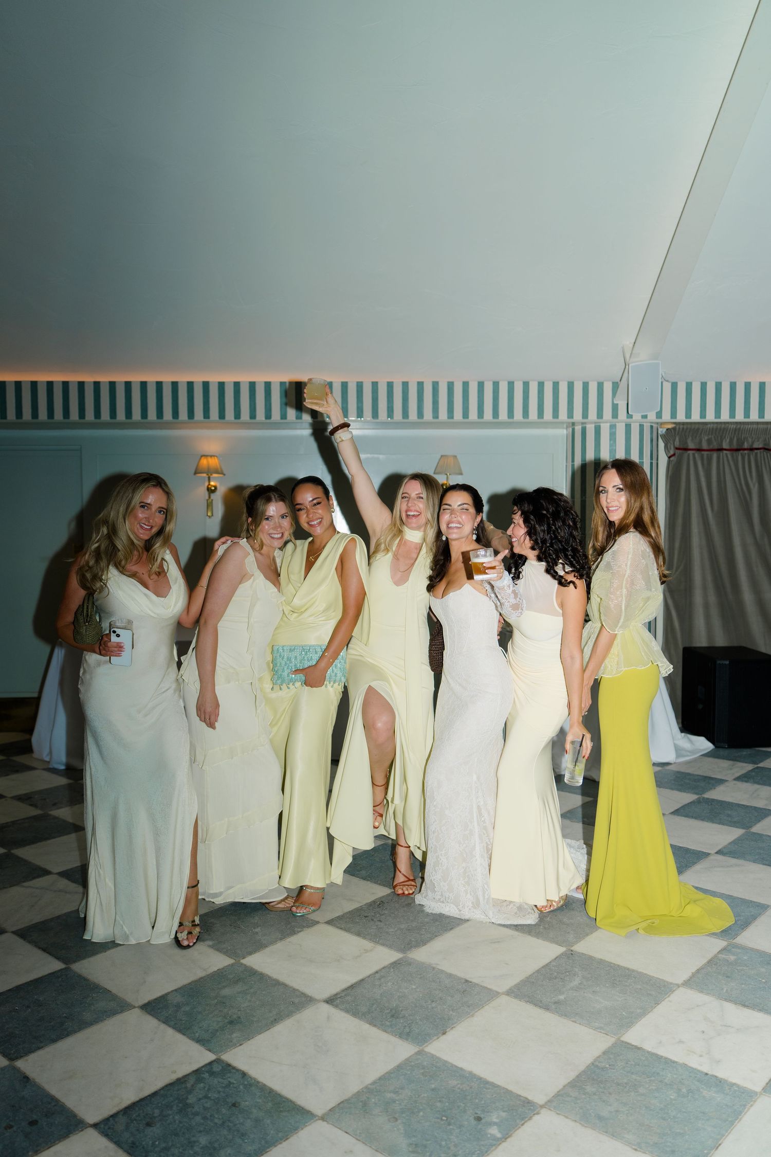 Group of bridesmaids and wedding guests celebrating in yellow and white dresses on a dance floor.