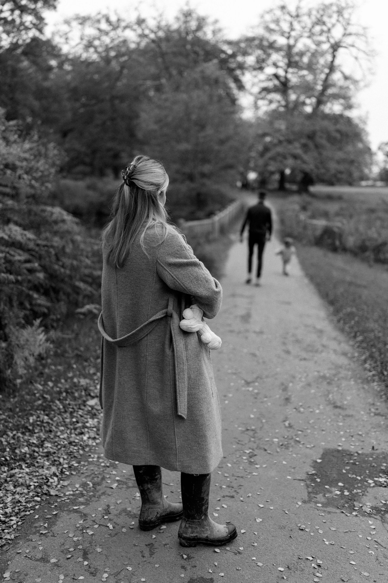 Black and white photo of a figure in a coat walking down an autumn path.