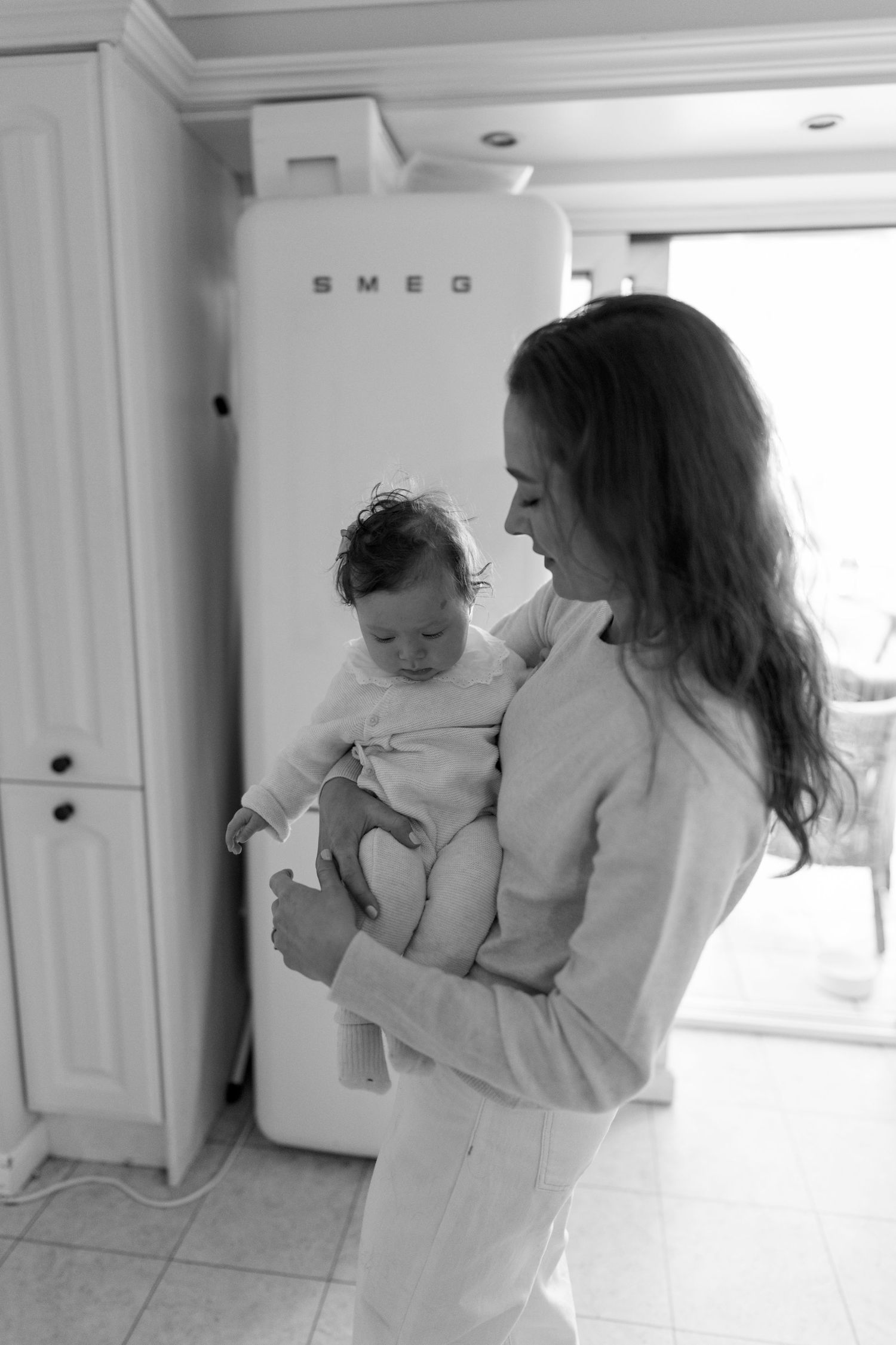 Mother and baby sharing playful moments in bright white kitchen.