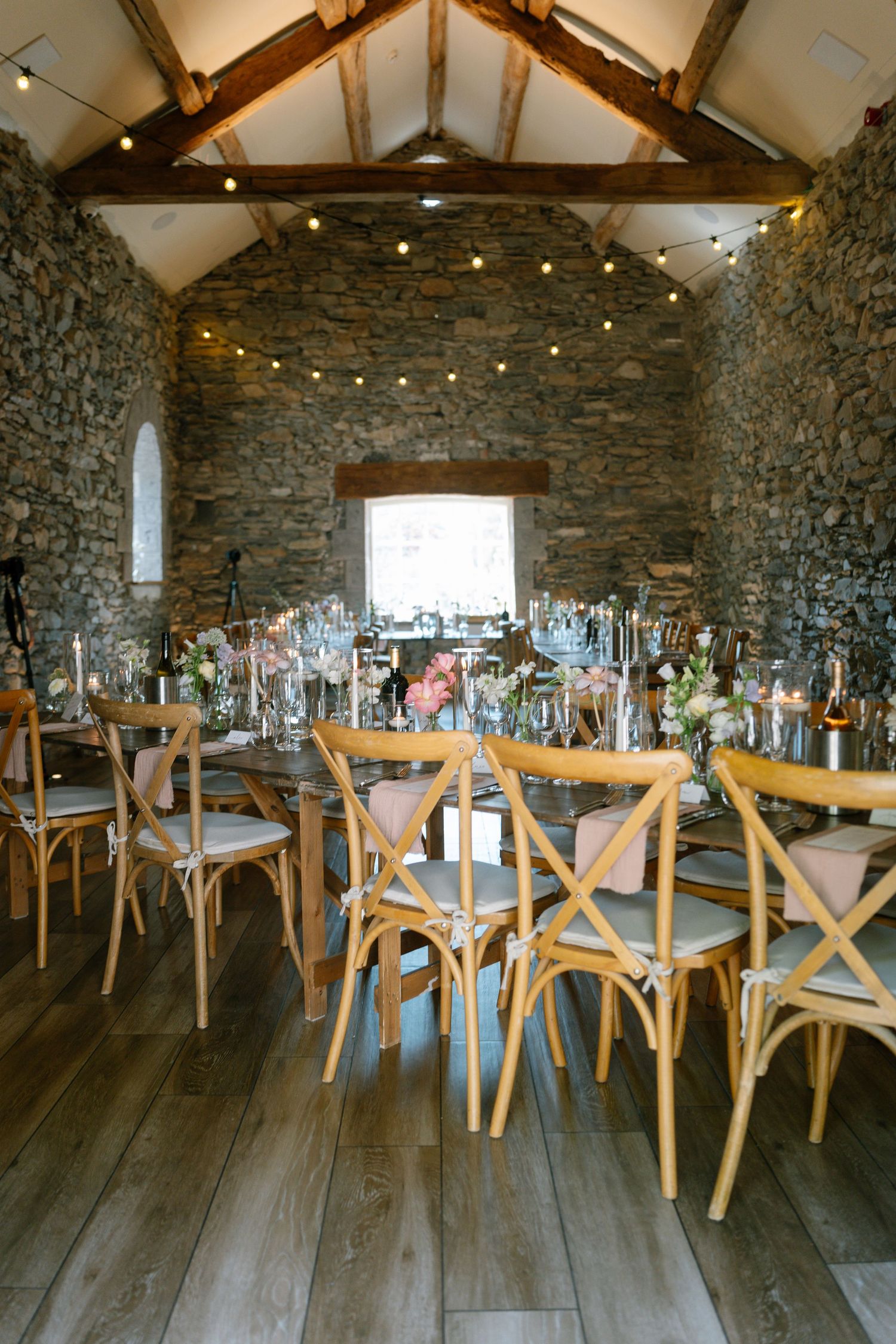 Wedding reception venue with cross-back chairs and string lights in rustic stone building.