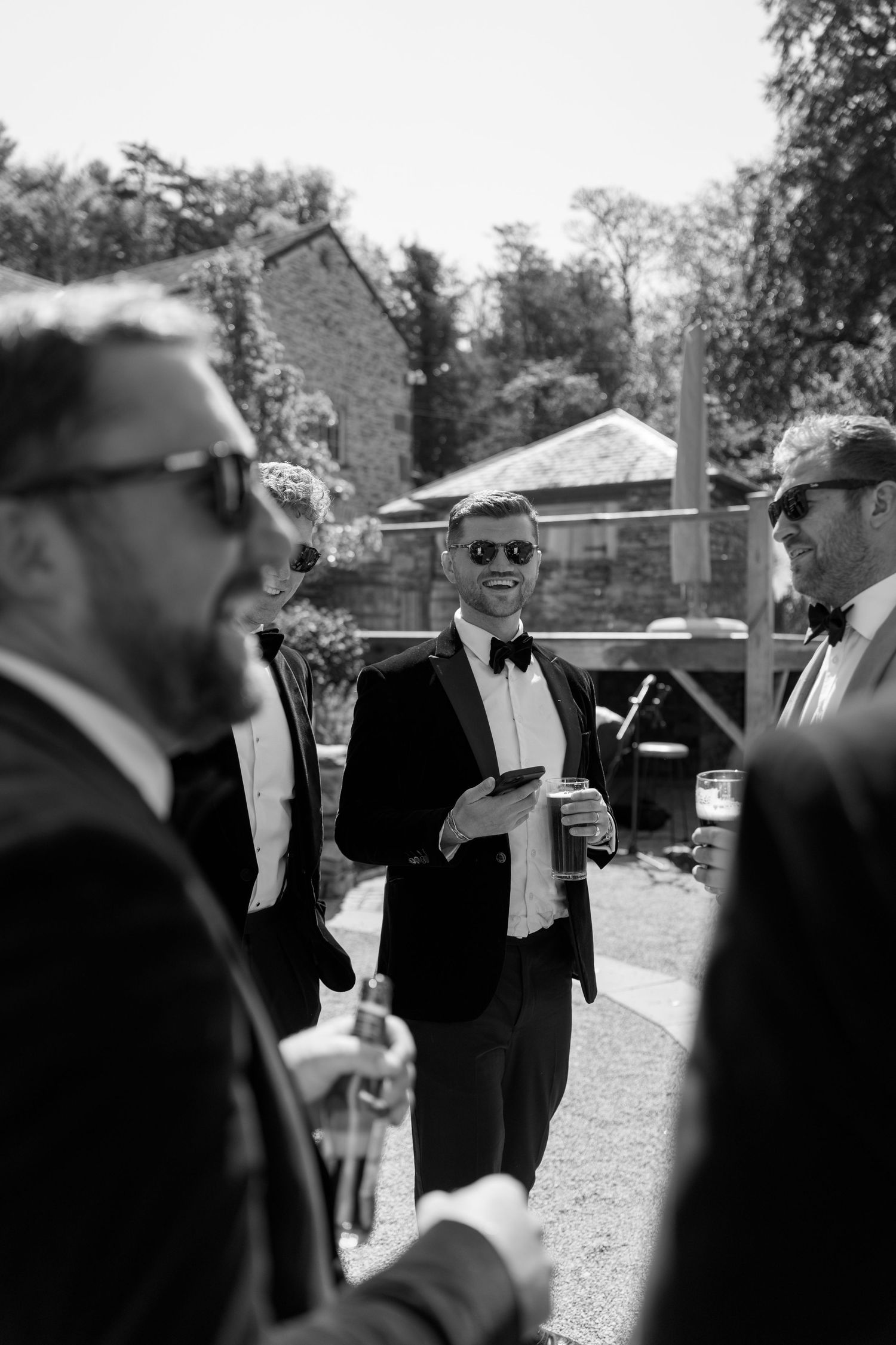Group of men in formal attire gathered outdoors on a sunny day.