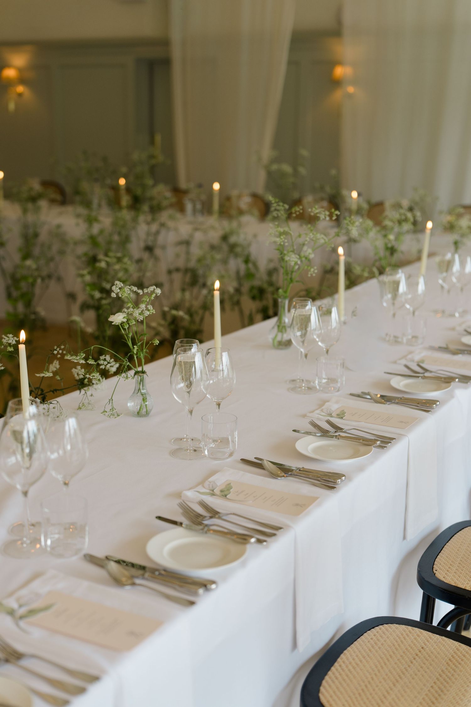 Elegant wedding reception table set with white linens, taper candles, and delicate wildflower arrangements.
