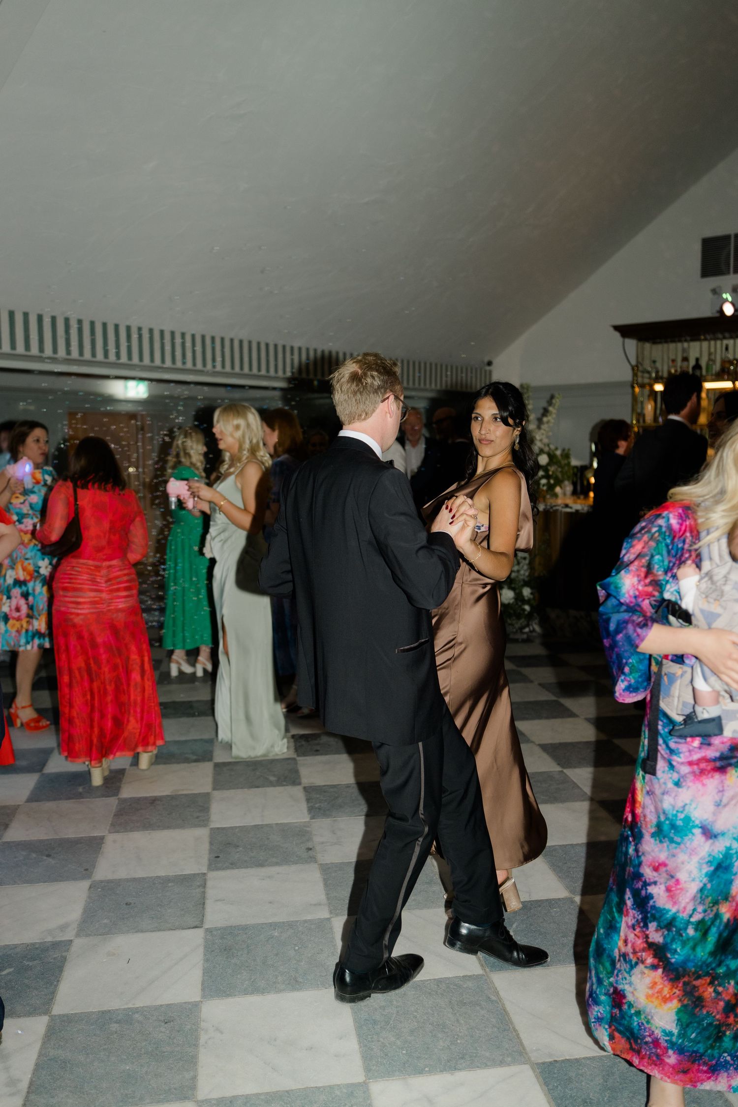 Wedding guests dancing and socializing on a checkered floor at a lively wedding reception.