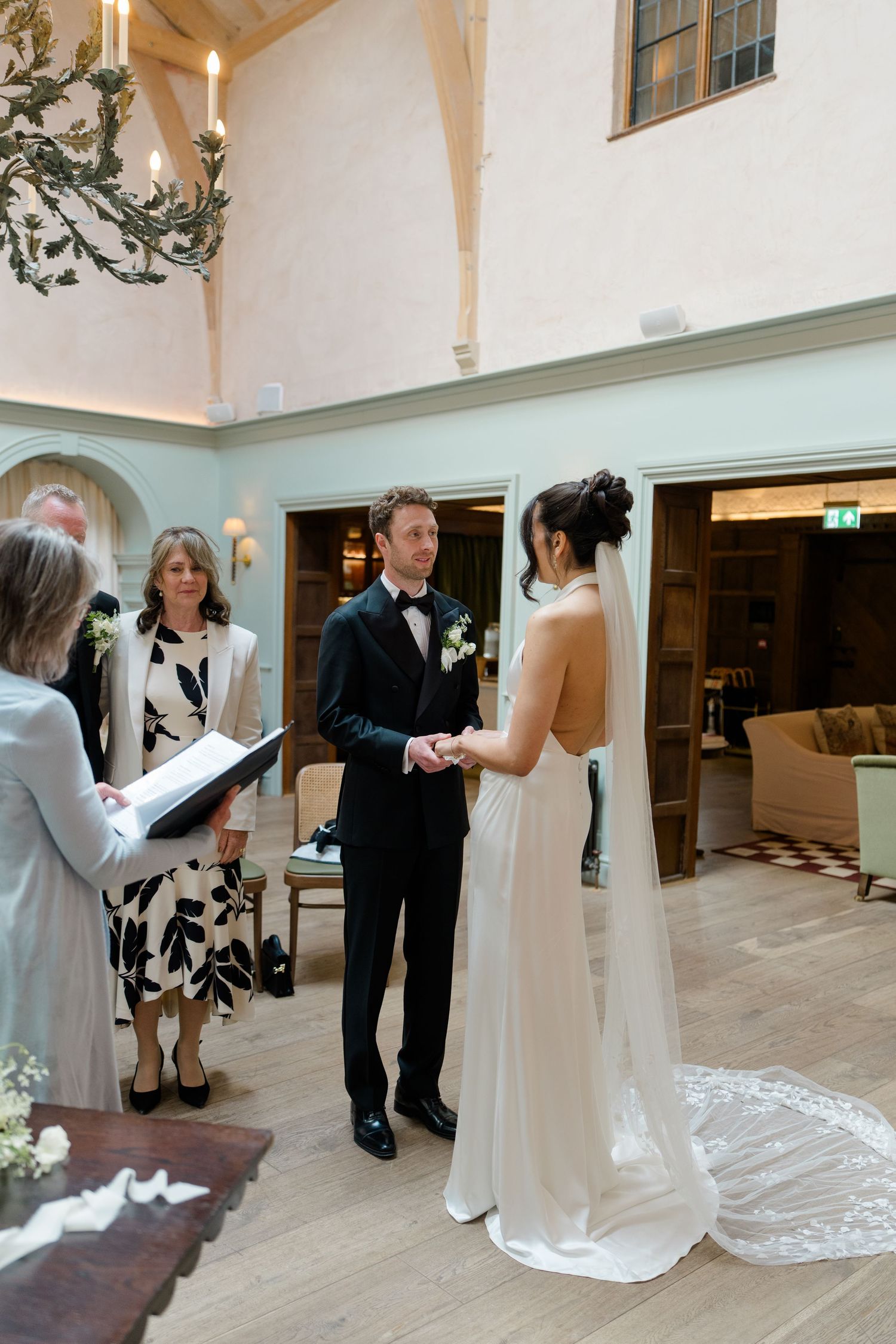 Bride and groom exchanging vows indoors in an elegant venue with a chandelier and wooden floors.