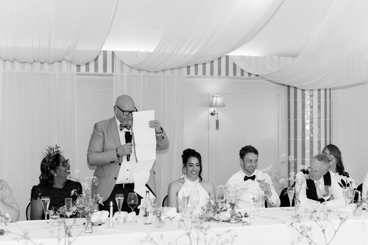 Black and white photo of father of bride giving speech at elegant marquee wedding reception.