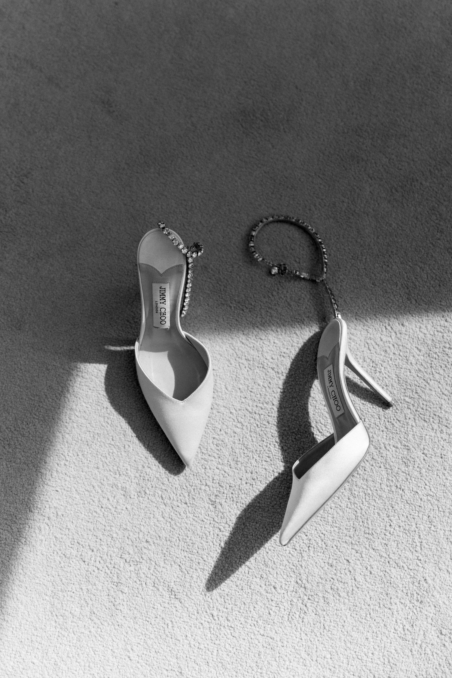 Elegant white high heel shoes photographed with dramatic shadows on a light surface.