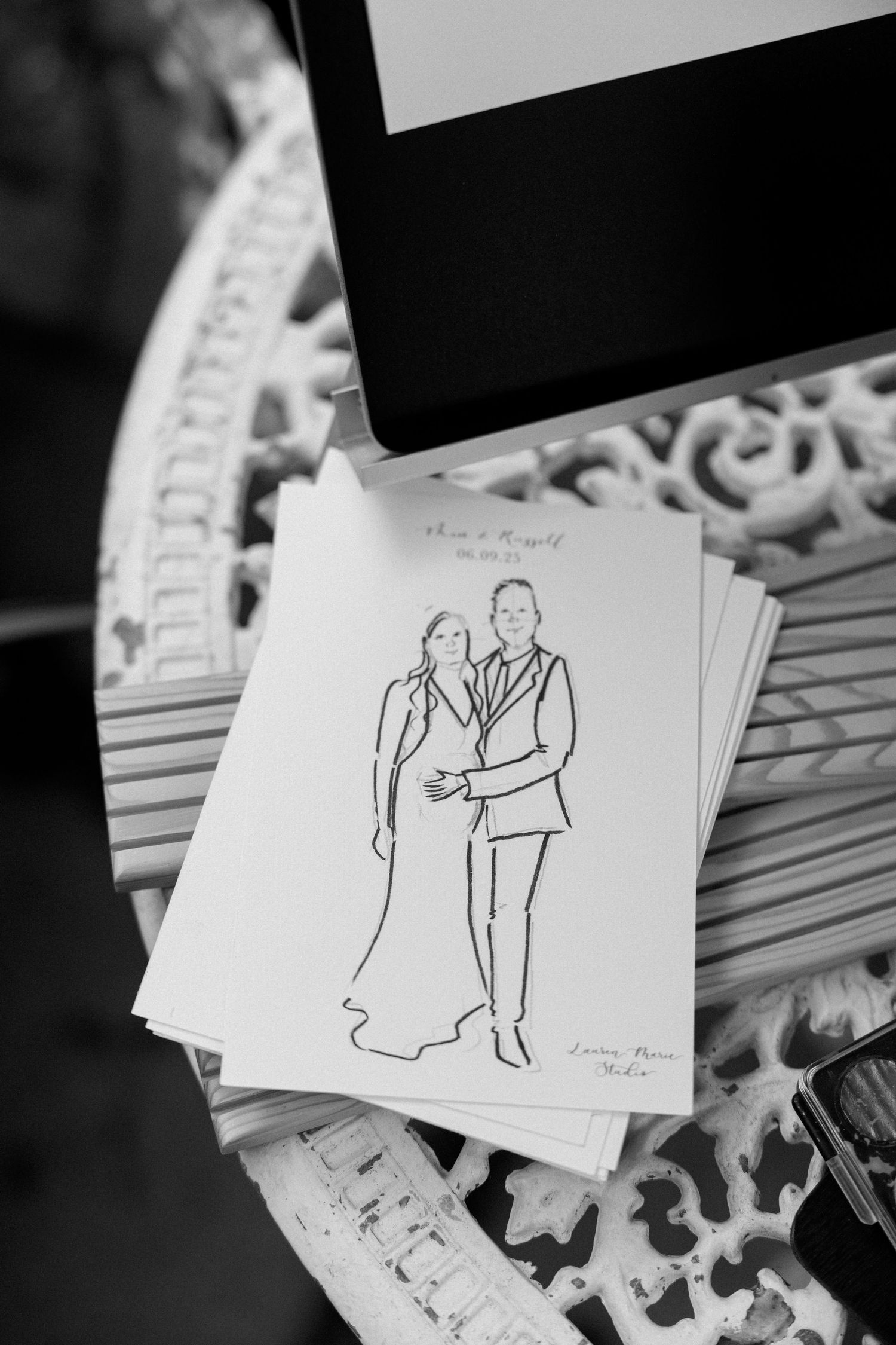 Black and white sketches of a couple displayed on decorative paper at a wedding.