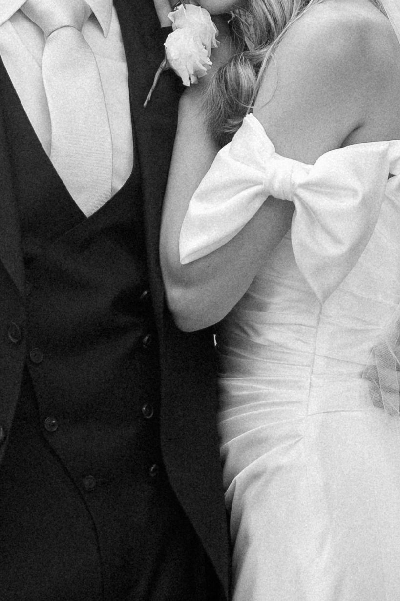 Black and white close-up of elegant wedding attire showing dress details and formal wear.