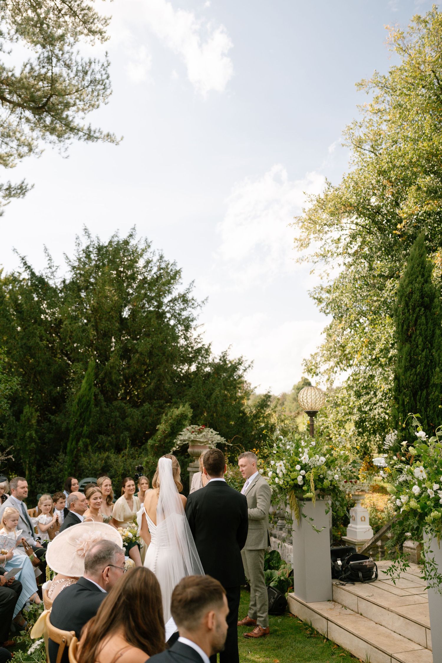 Wedding ceremony guests seated on a terraced garden lawn during an outdoor celebration.