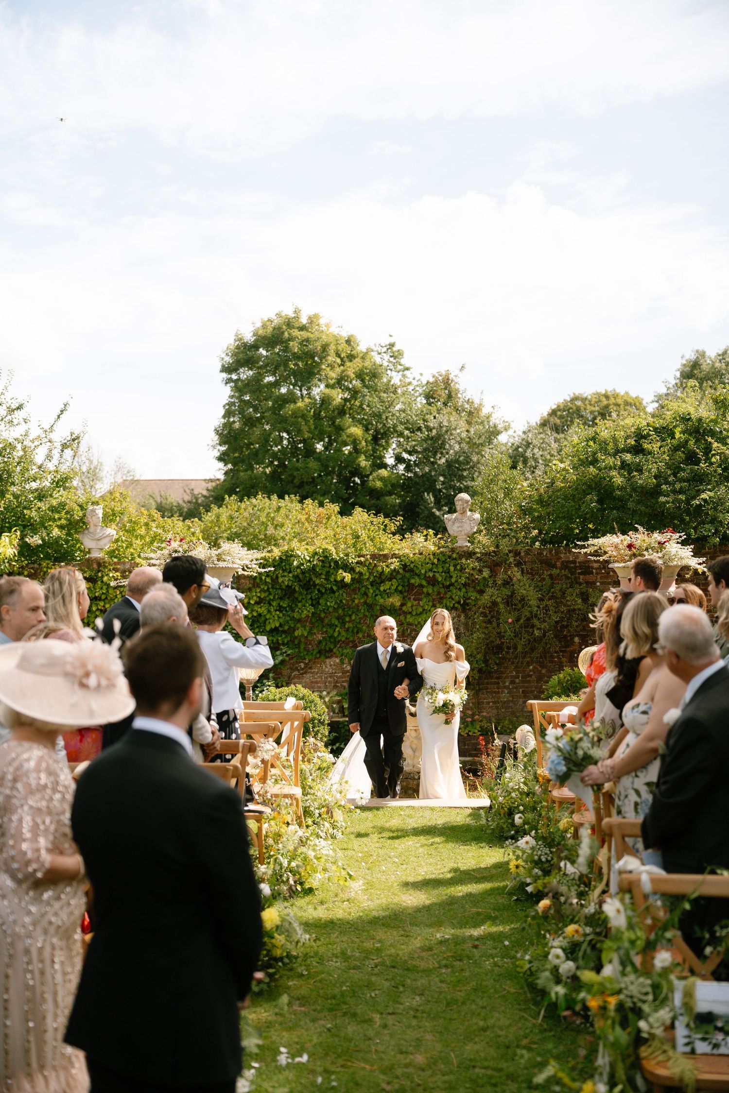 Wedding celebration in a sunlit garden with guests mingling among floral decorations.
