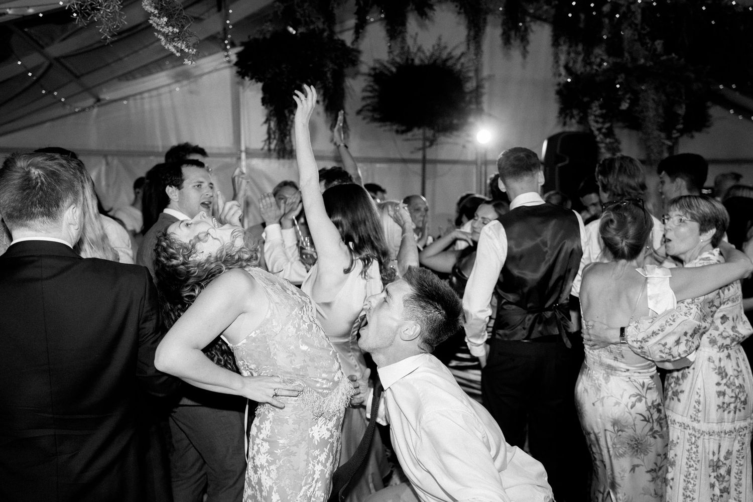 Black and white photo of guests dancing and celebrating at a lively wedding reception.