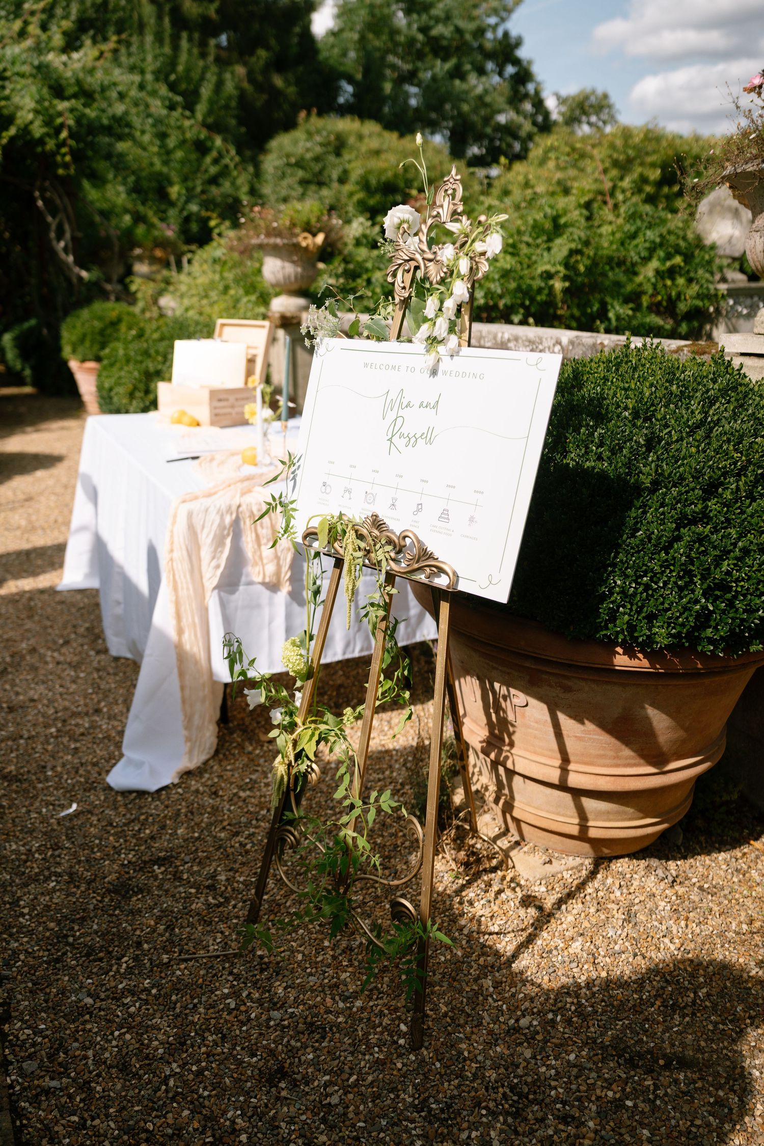 Wedding reception setup with white tablecloths and signage in a formal garden.