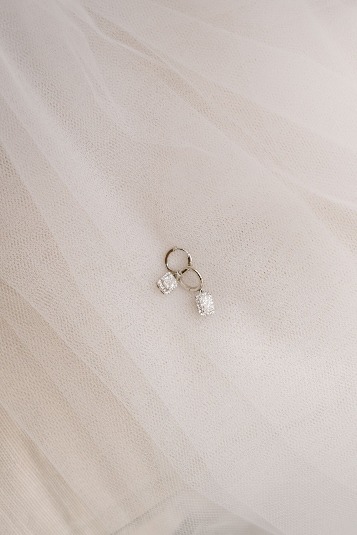 Wedding rings and diamond engagement ring photographed on delicate white tulle fabric.