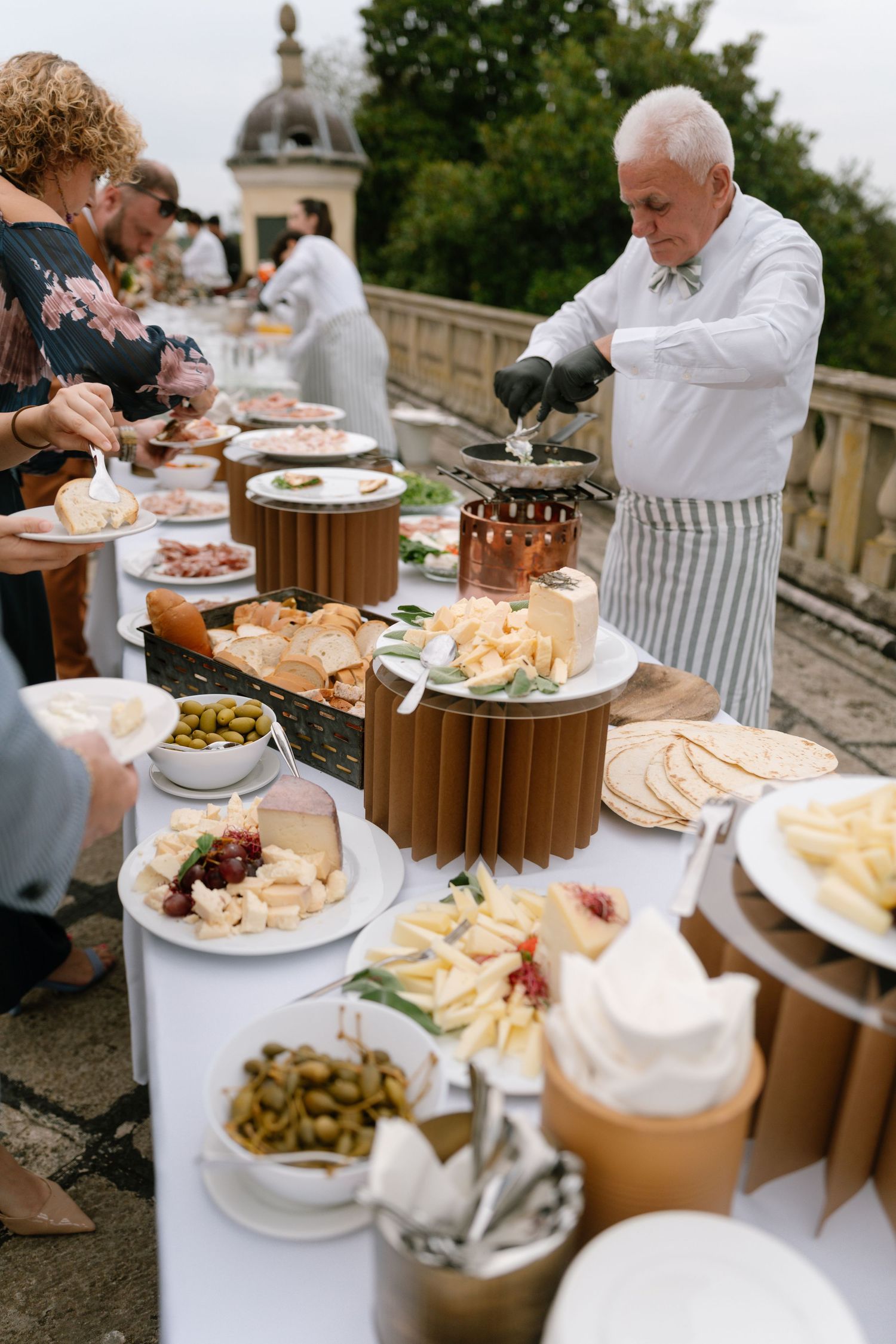 Elegant outdoor wedding buffet with a chef serving food on a stone terrace.