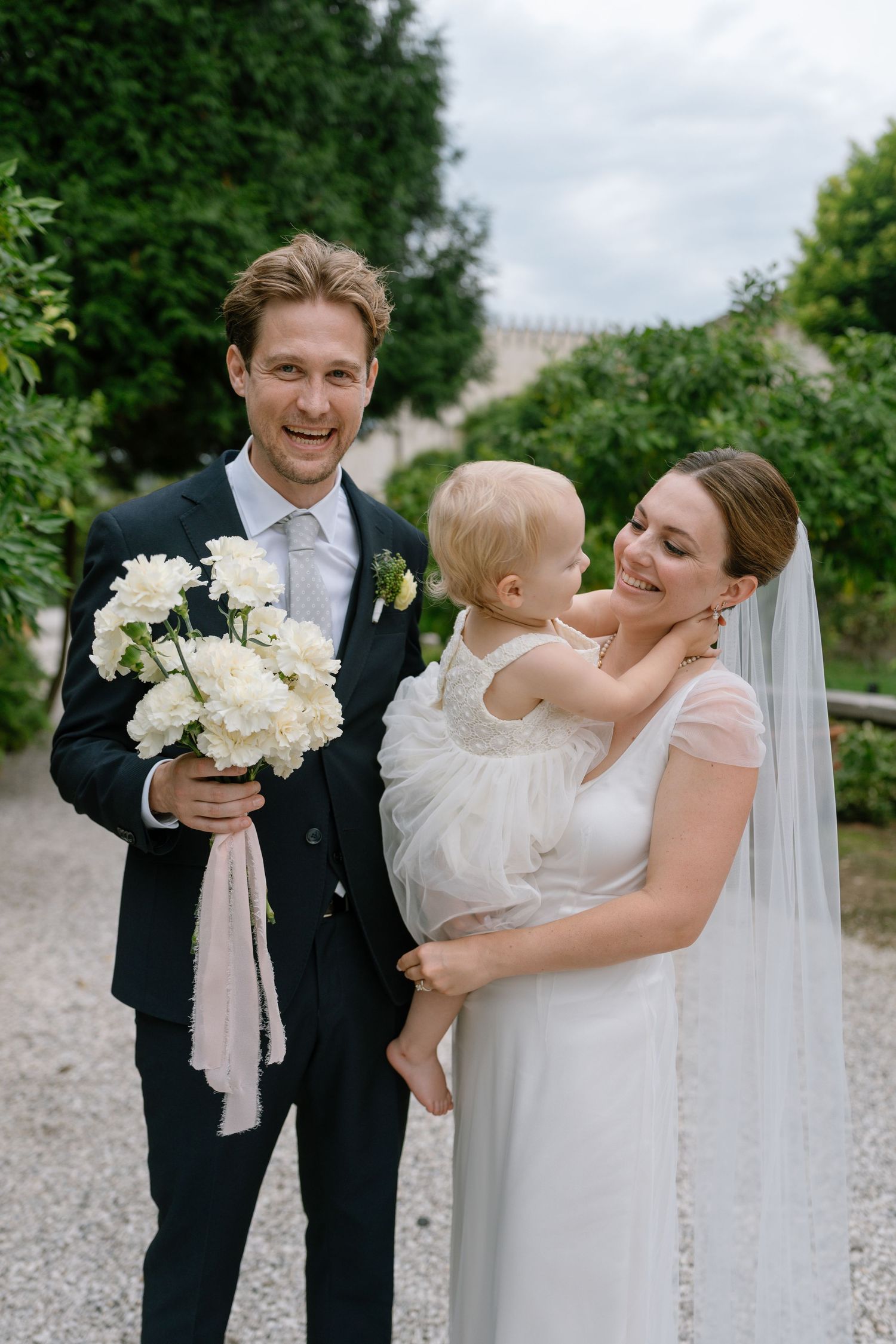 Joyful wedding moments shared on a gravel path with white flowers and formal attire.