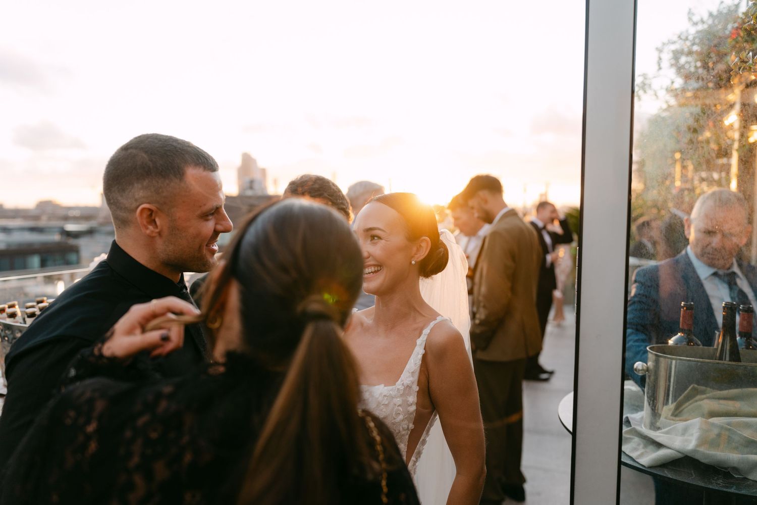Wedding guests mingling at a rooftop venue during golden hour.