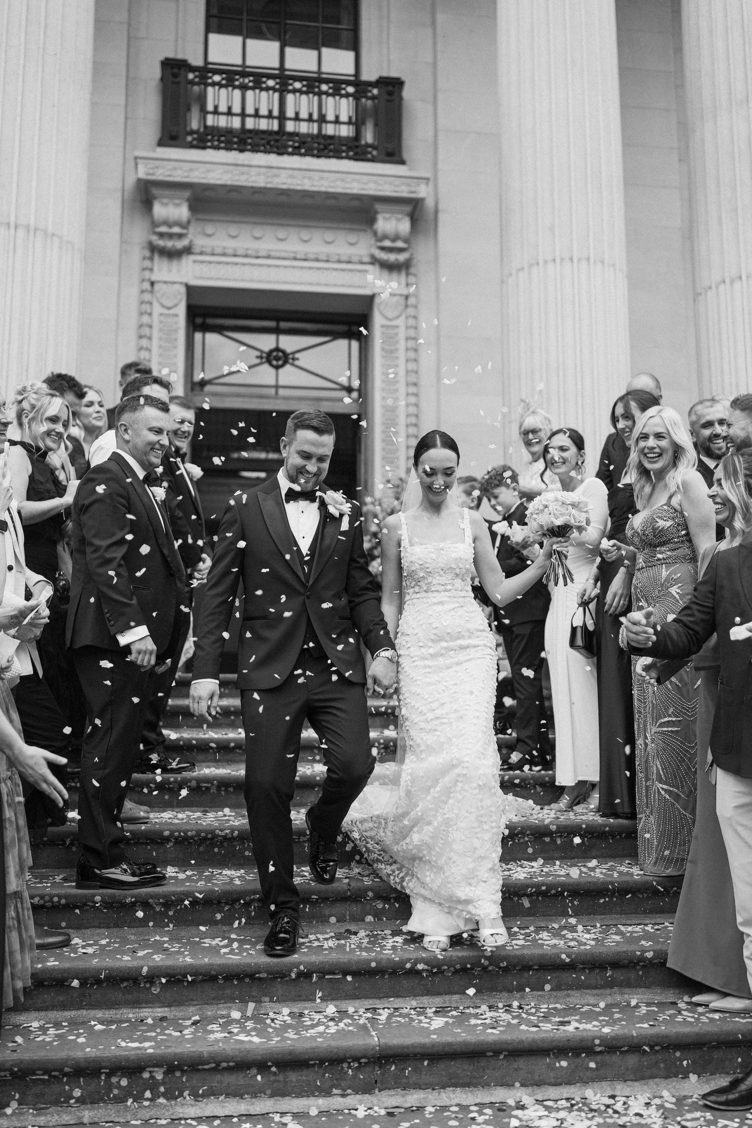 Guests shower newlyweds with confetti on classical building steps.