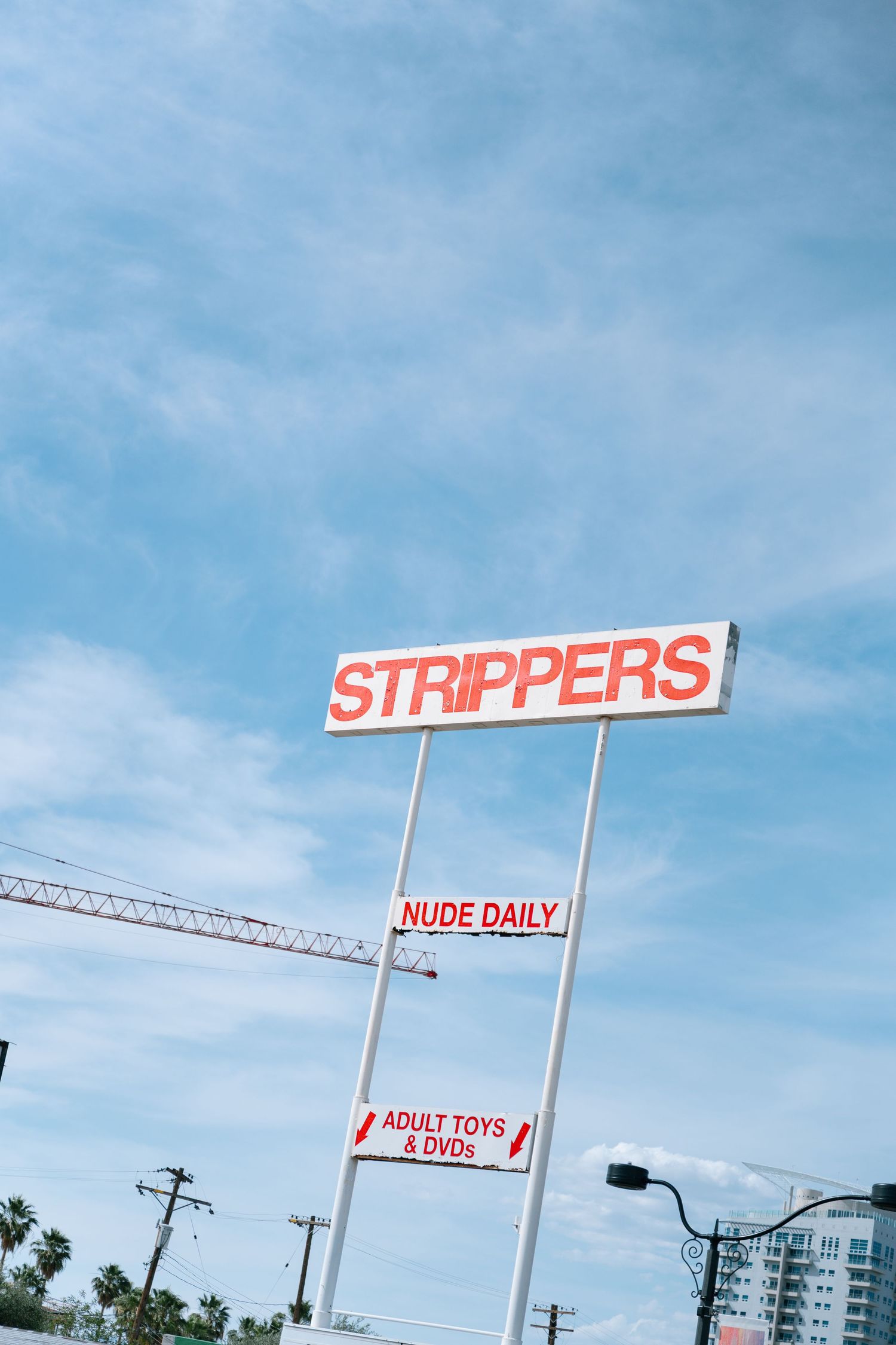 Adult entertainment signage against a bright blue Las Vegas sky.