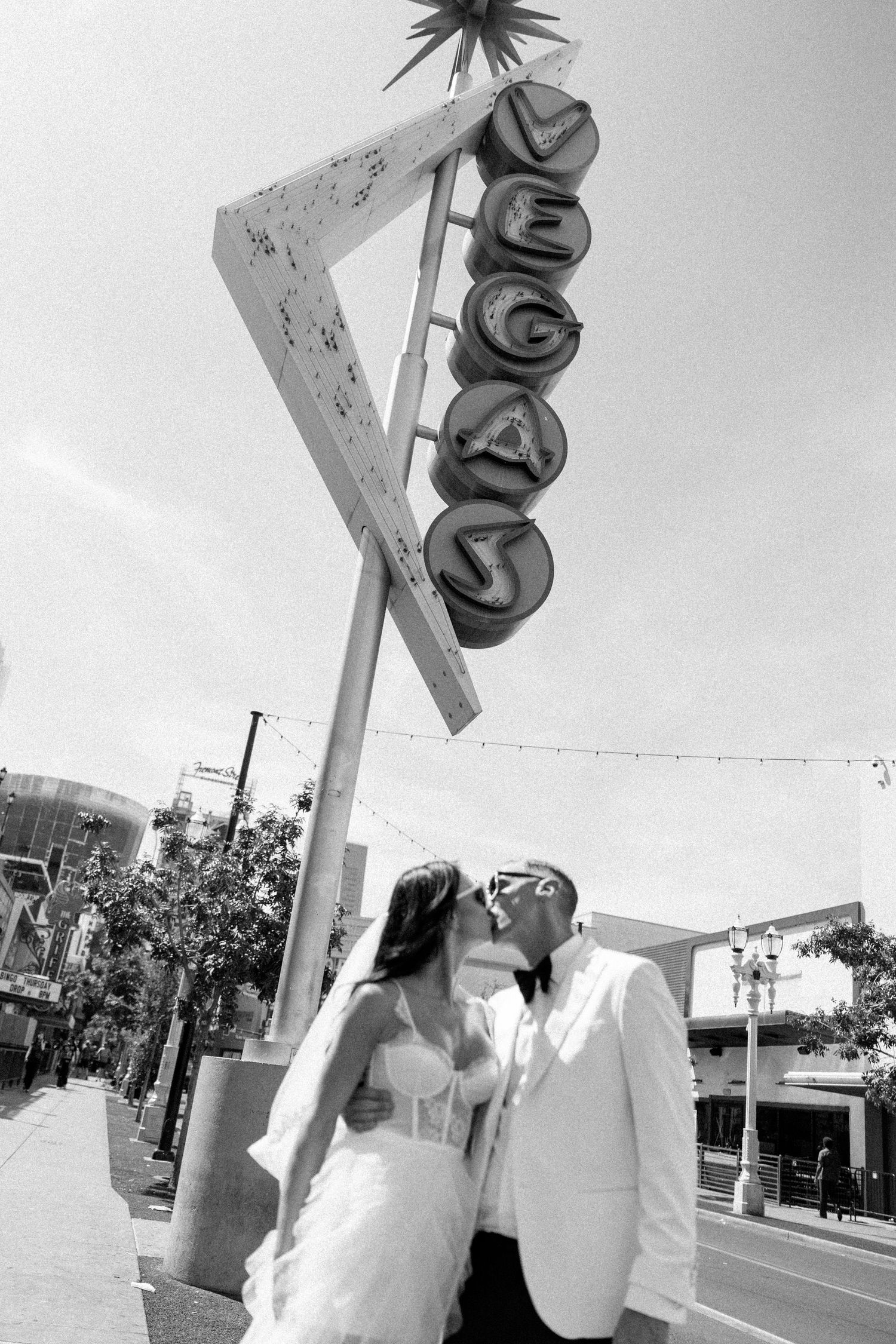 Black and white photo of newlyweds sharing intimate moment under vintage Vegas sign.