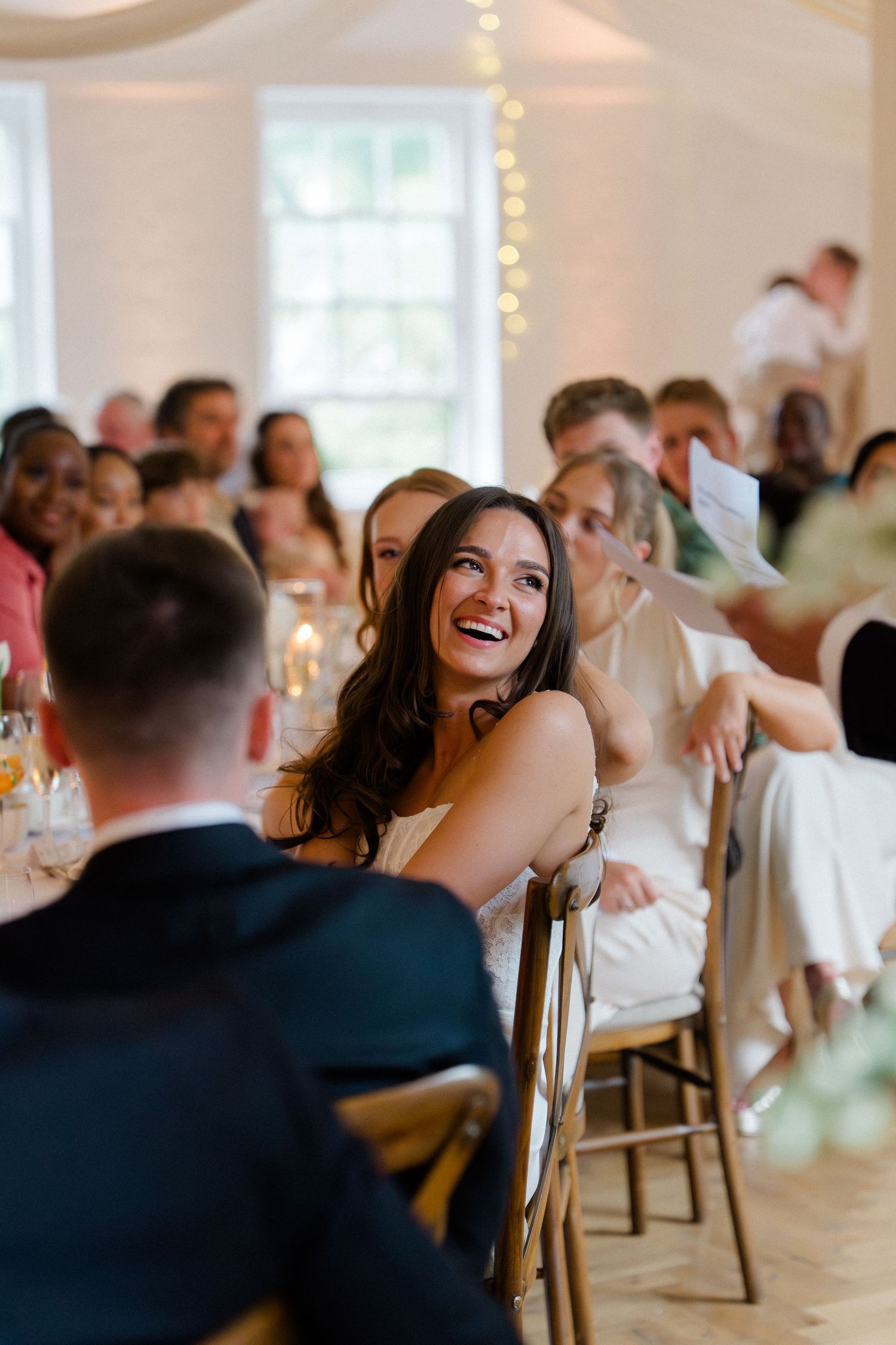 Radiant bride laughing joyfully at her wedding reception while seated at the head table with guests.