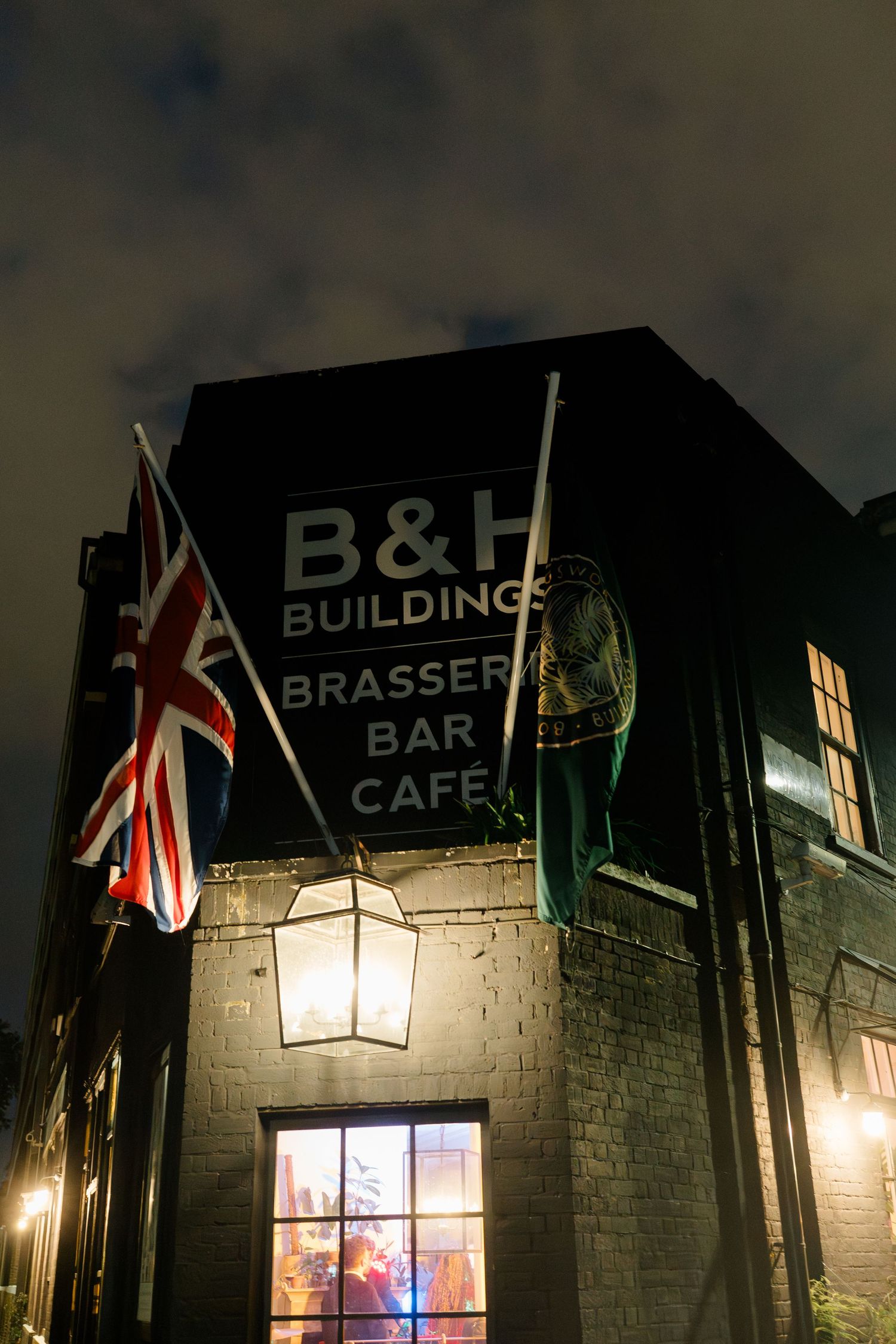 B&H Buildings Brasserie Bar Cafe exterior at night with Union Jack flag and vintage lantern lighting.