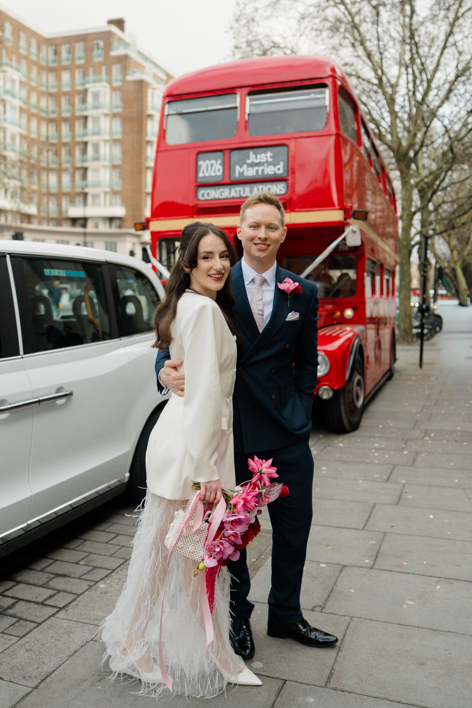 Newlyweds pose in front of a red London double-decker Just Married bus.