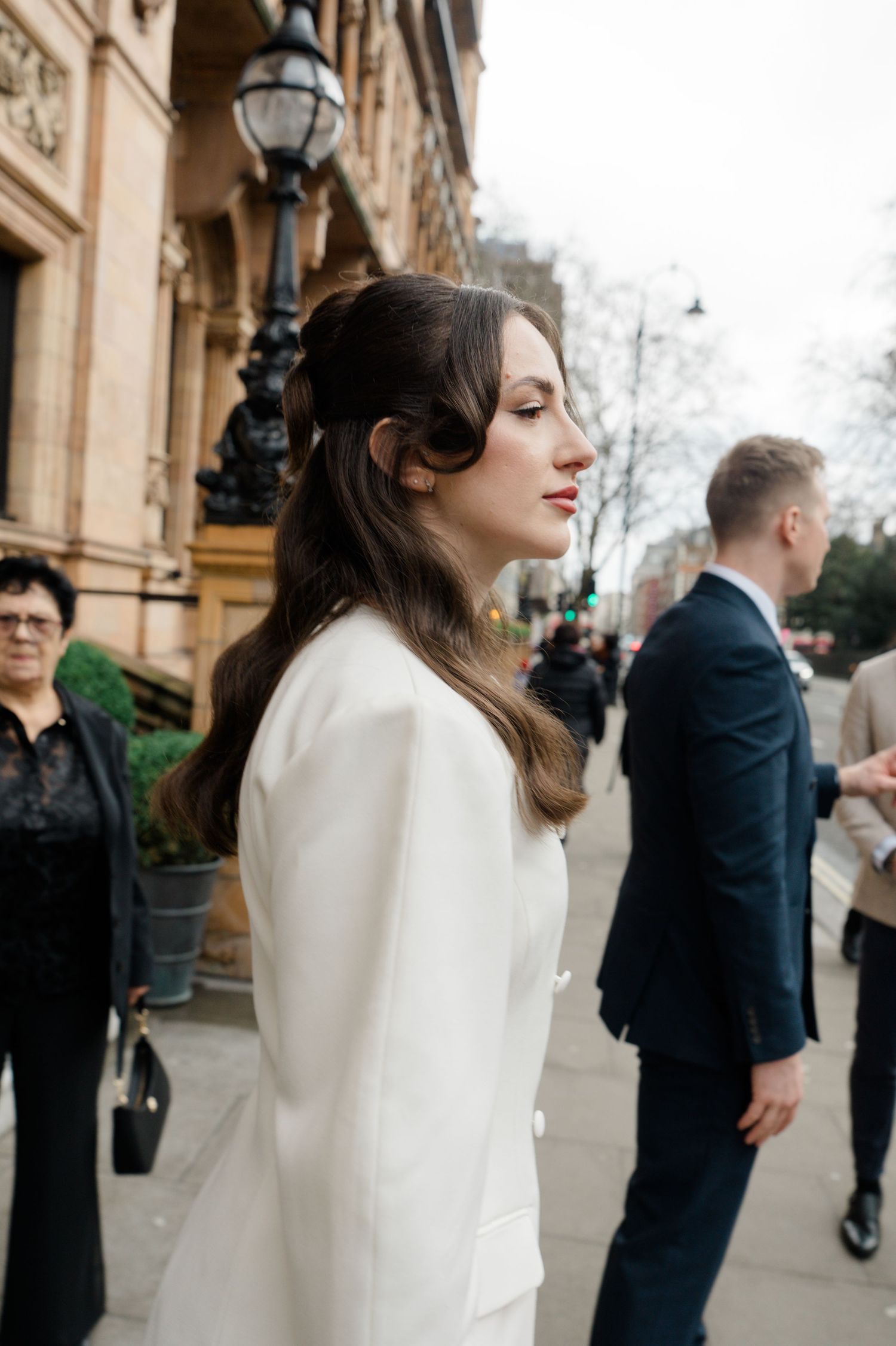 Elegant bride in white blazer dress with half-up hairstyle on a city street.