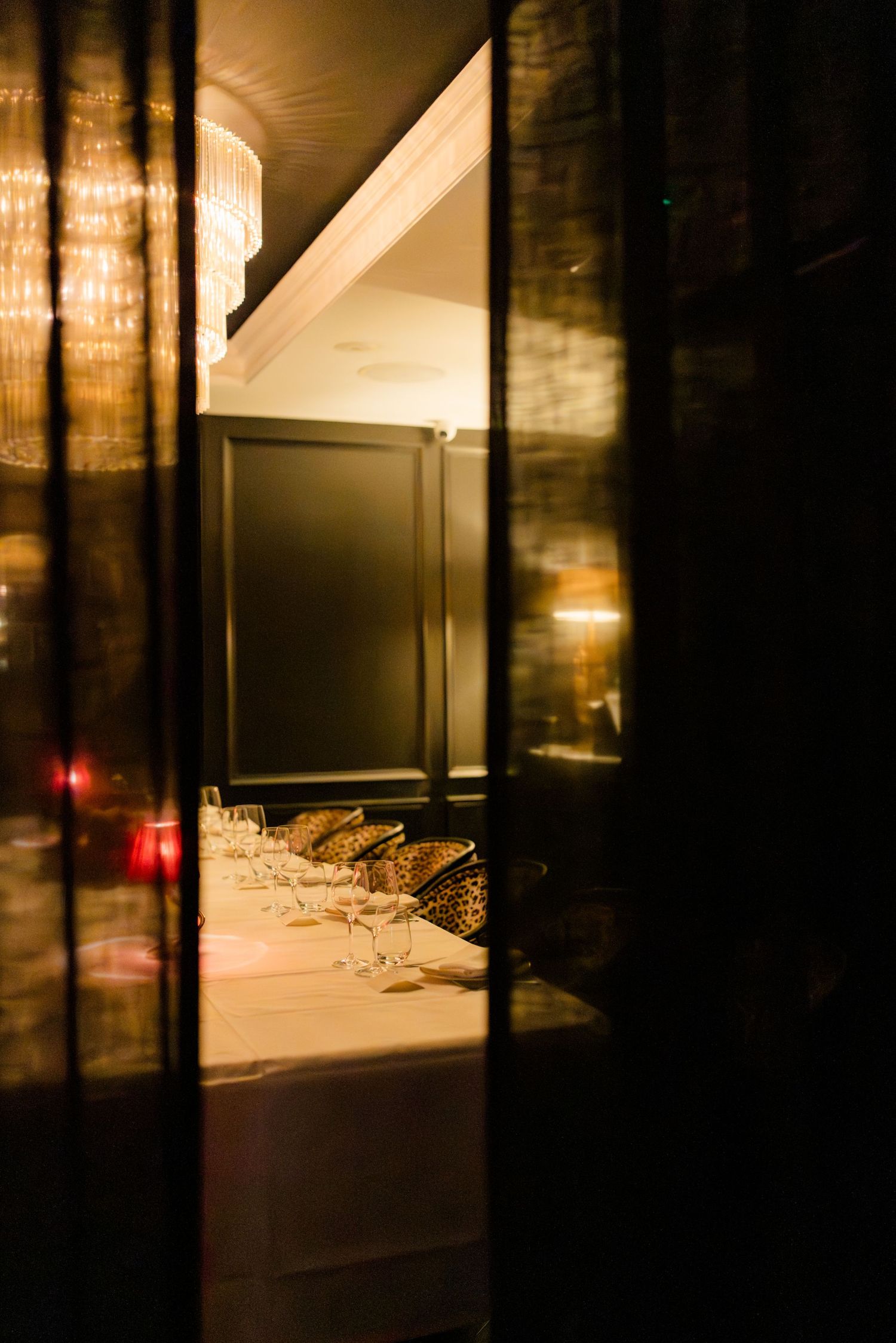 Warm atmospheric view through dark curtains of elegantly set dining table with wine glasses in dimly lit restaurant.