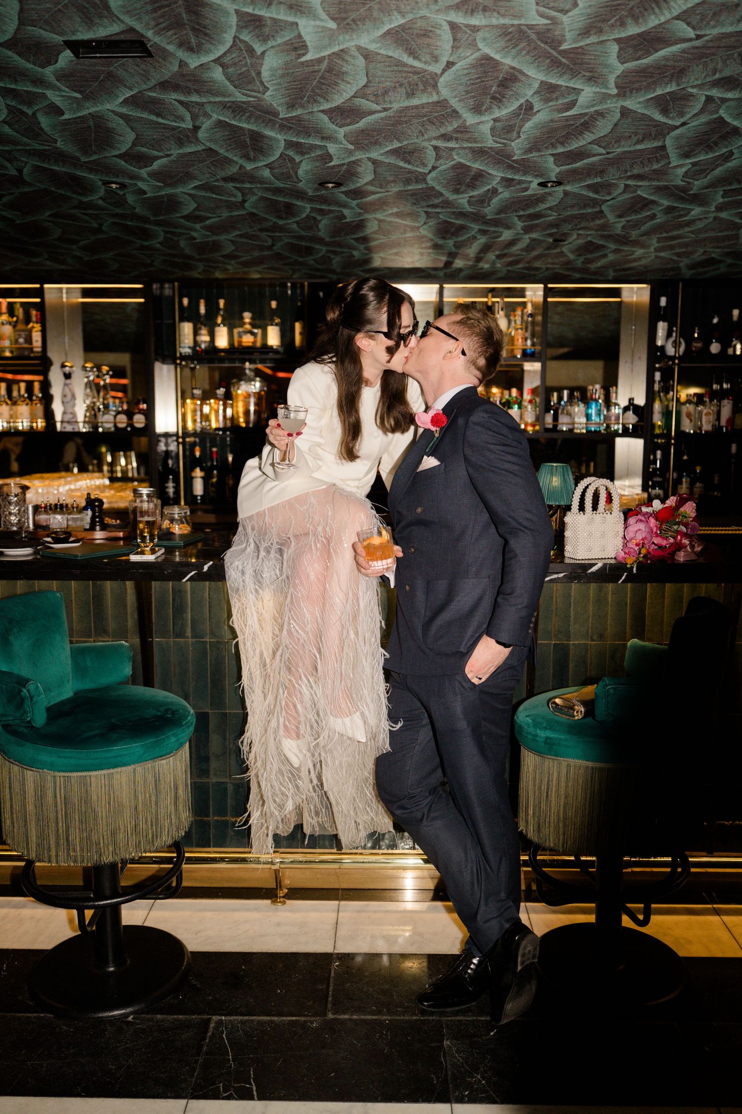 Bride and groom sharing a kiss at a luxury bar, bride wearing a white feathered wedding dress.