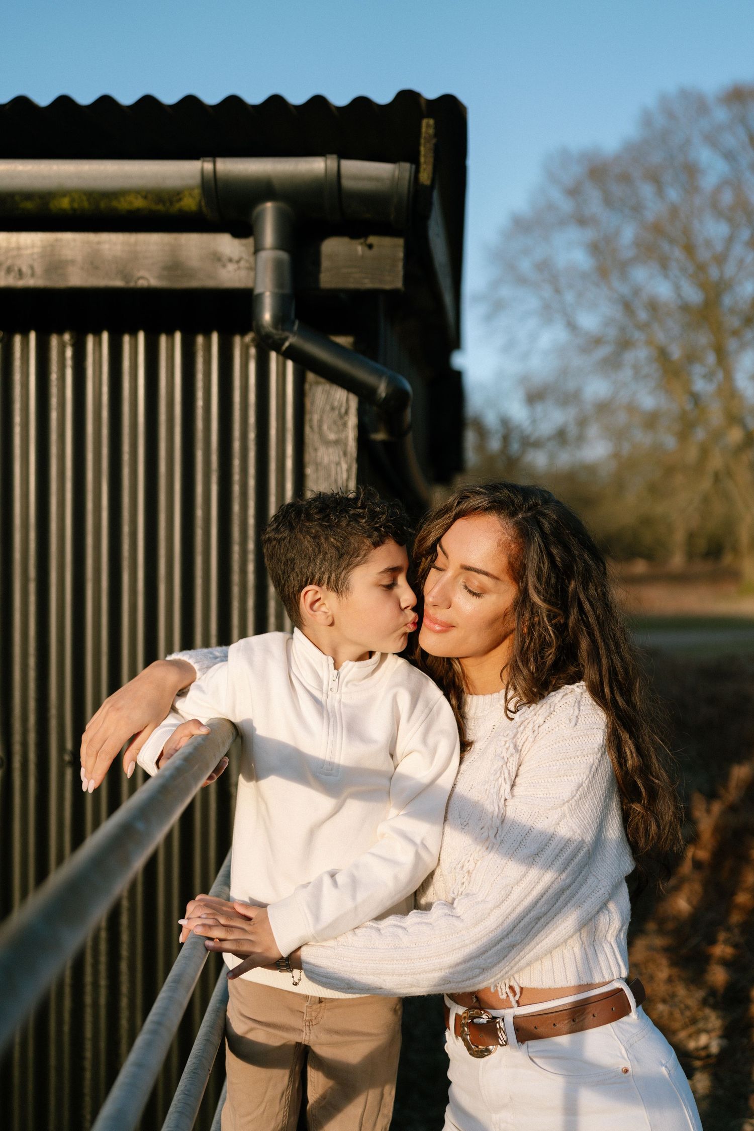 Two people in white outfits sharing an intimate moment near a wooden fence.