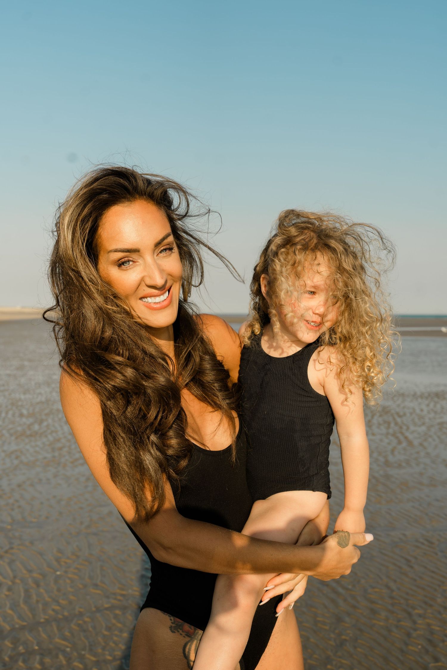 People in black swimsuits laughing and embracing on a sunny beach.
