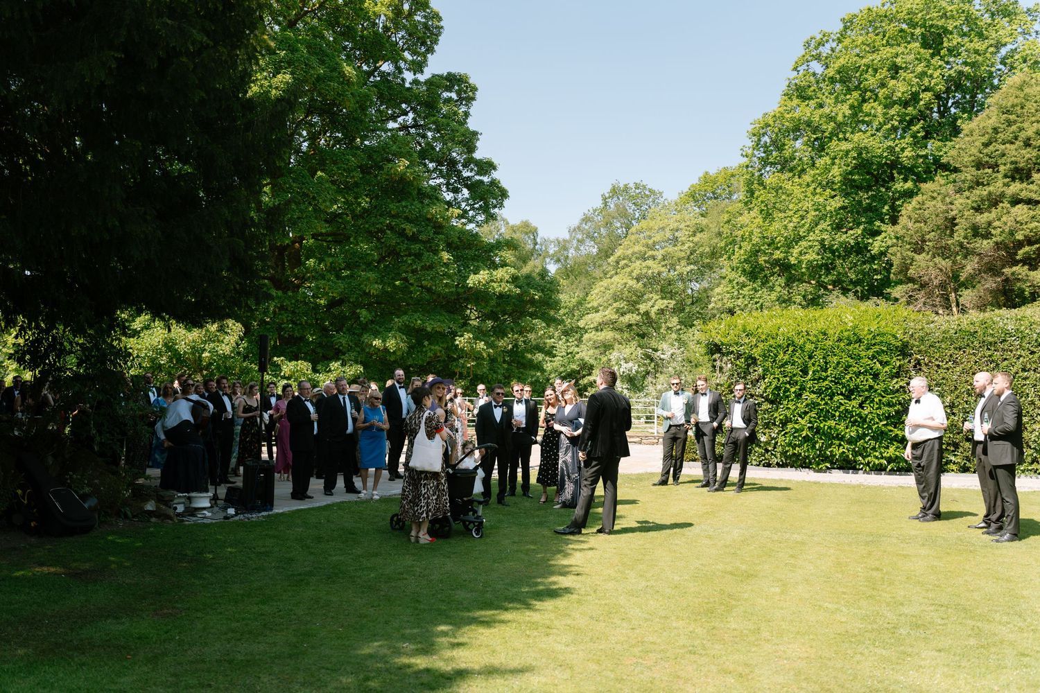 Wedding guests gather on a sunny lawn during an outdoor ceremony.