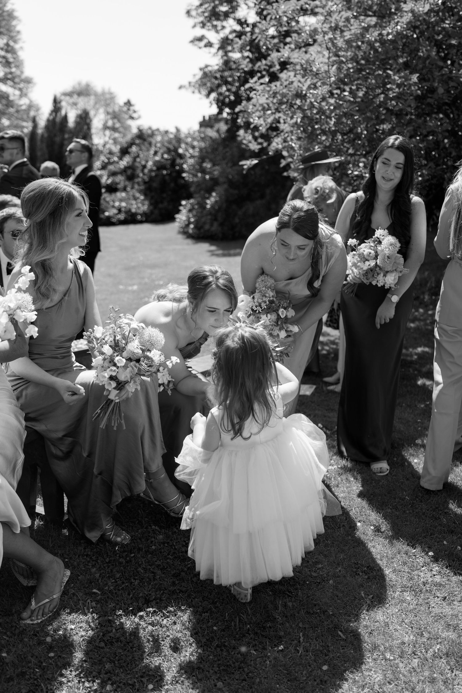 Young flower girls in white dresses gather on the lawn during a wedding celebration.