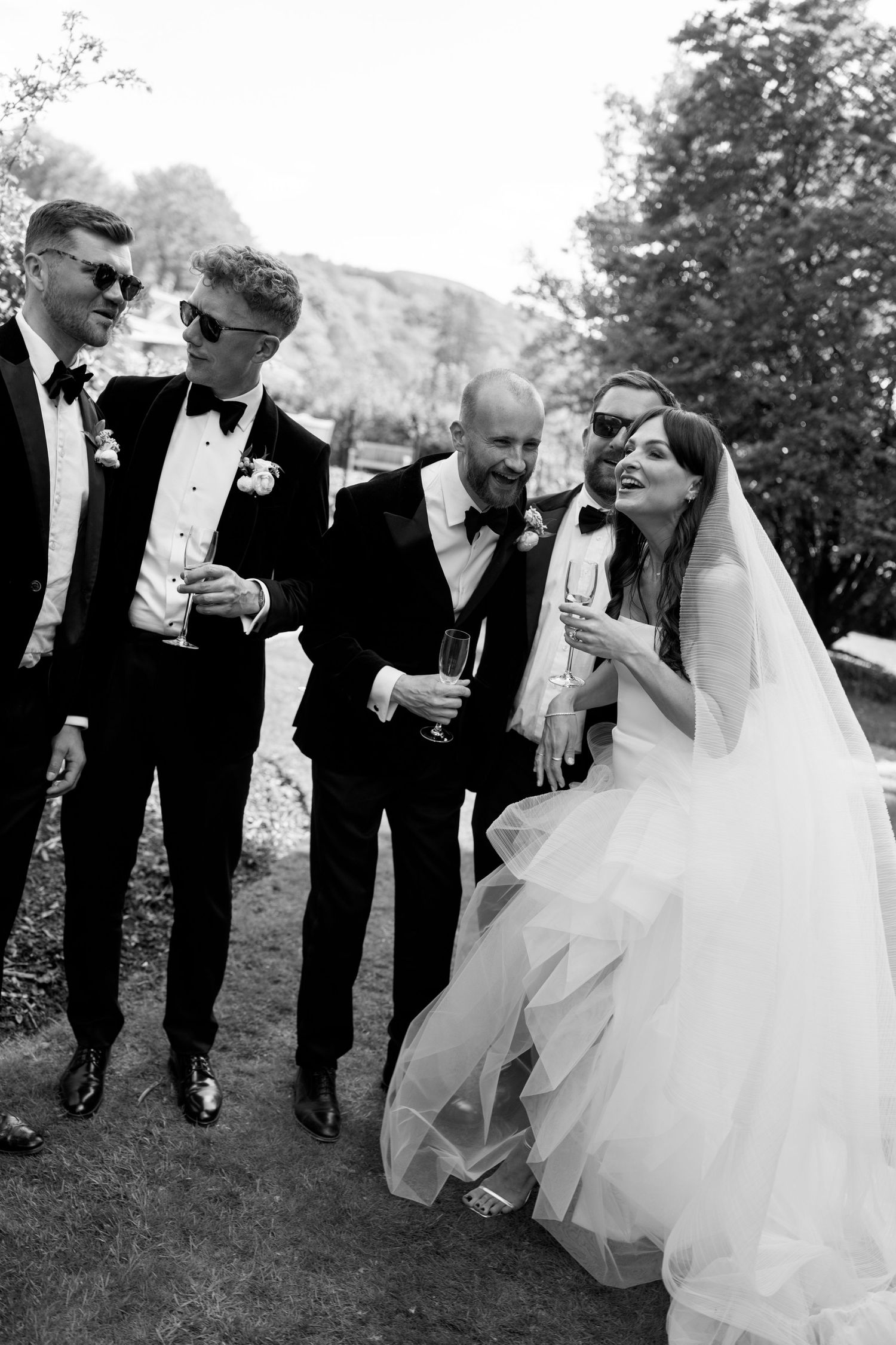Wedding party shares drinks and laughs while walking outdoors.
