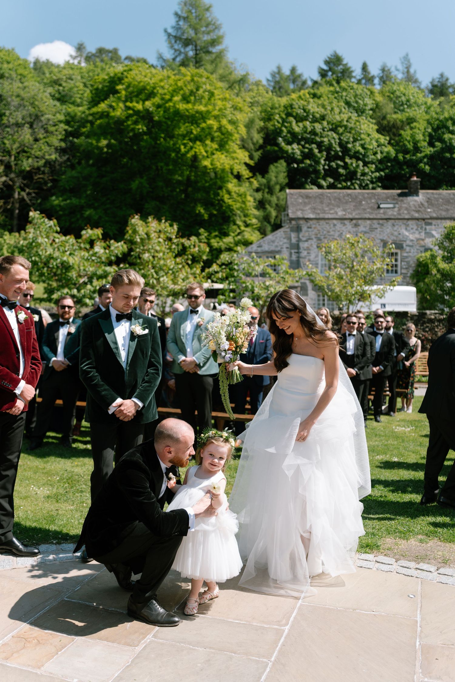 Wedding ceremony participants kneel on stone pathway during outdoor celebration.