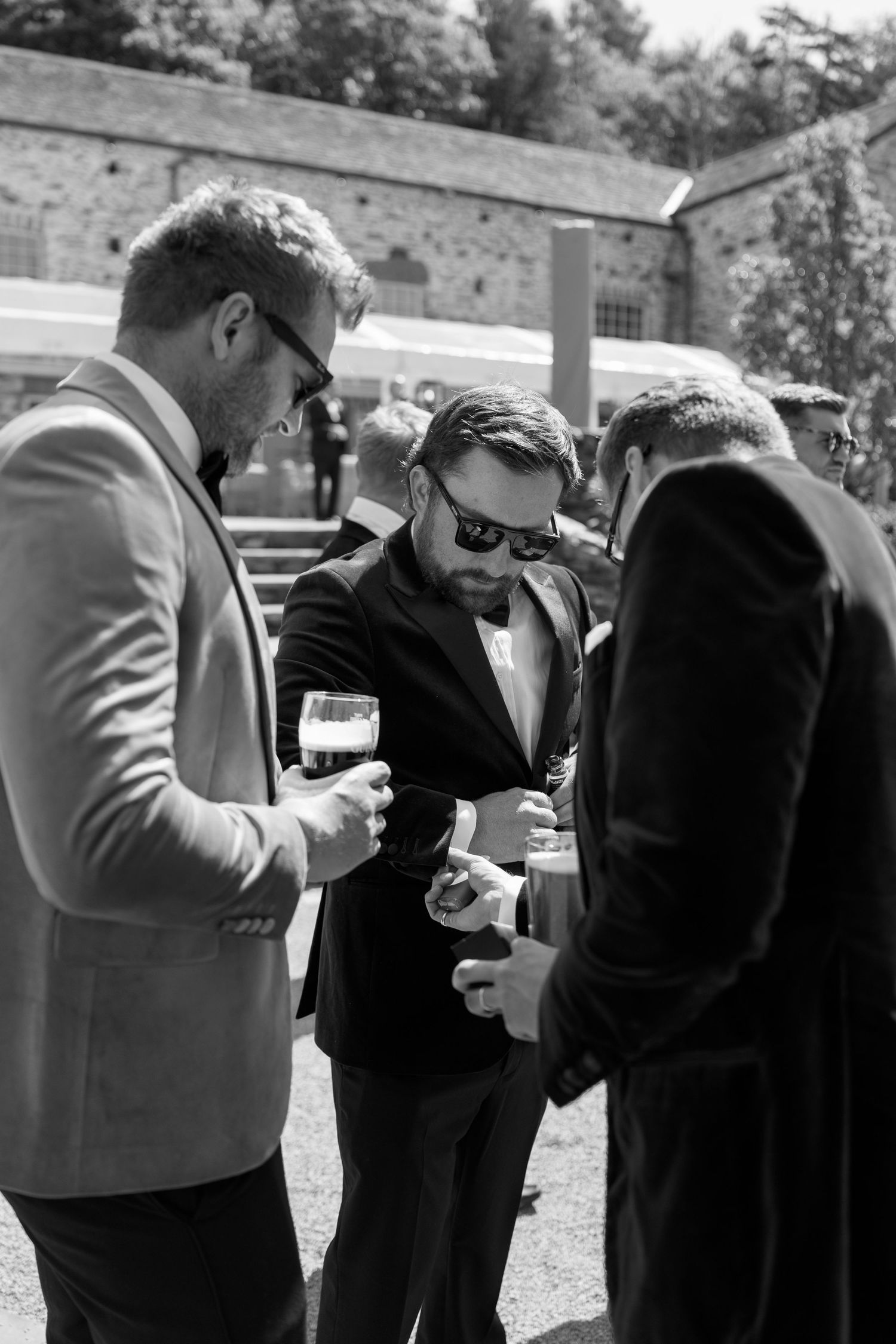 Wedding party members in formal attire helping each other with final adjustments outdoors.