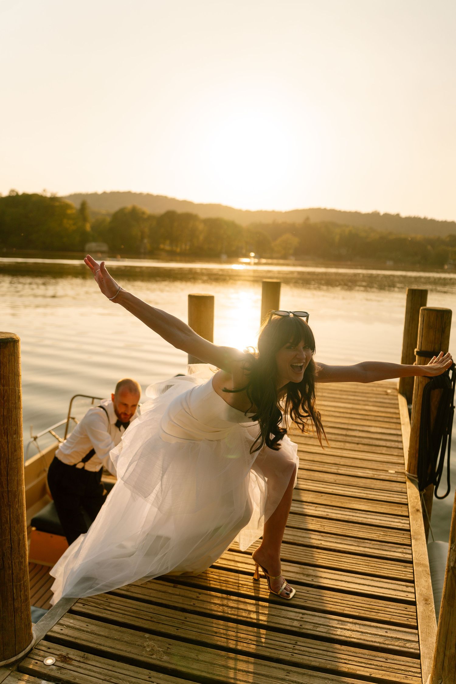 Couple striking dramatic poses on a lakeside dock during golden hour.