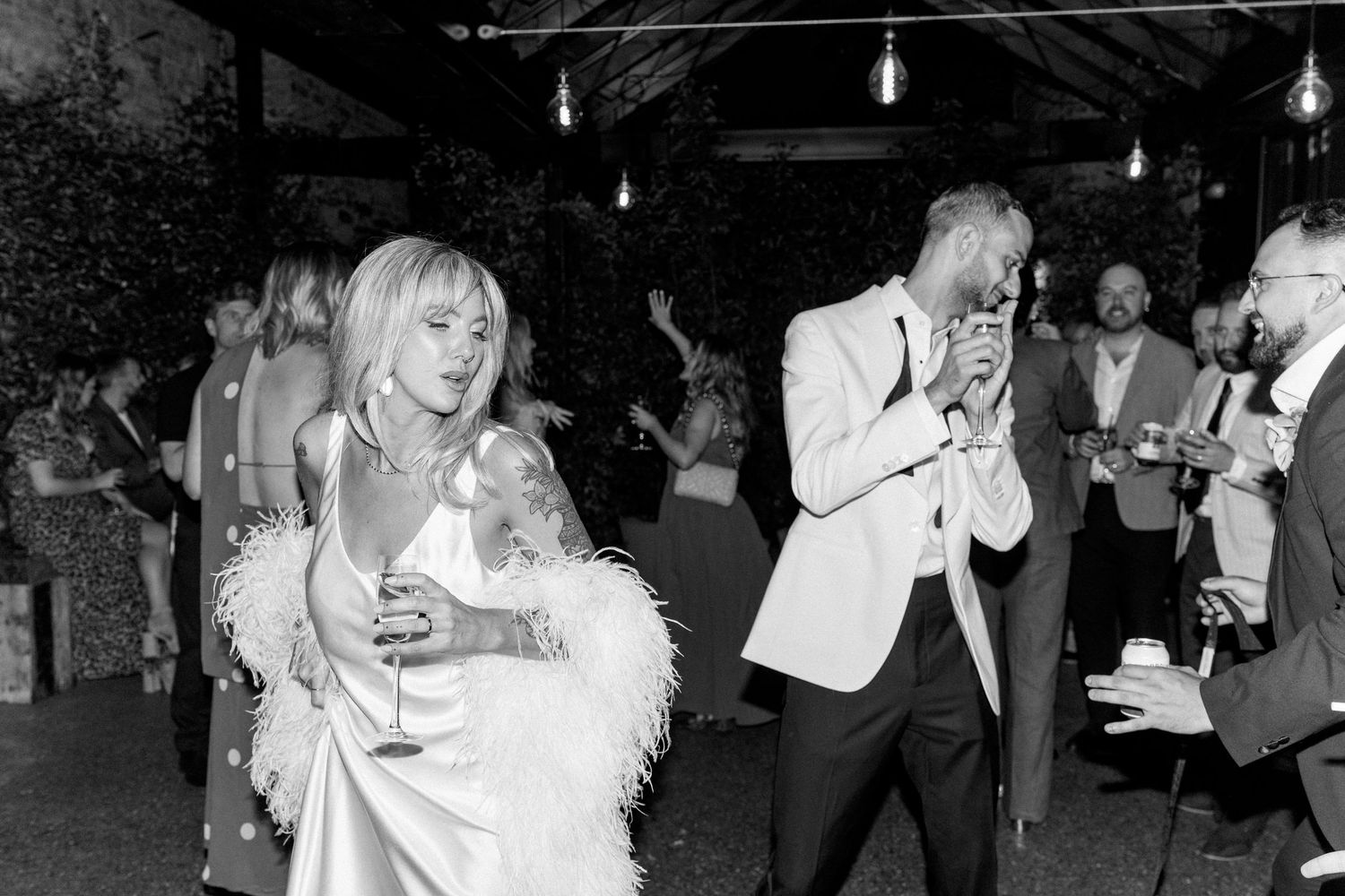Wedding guests dance and celebrate under string lights at an evening reception.